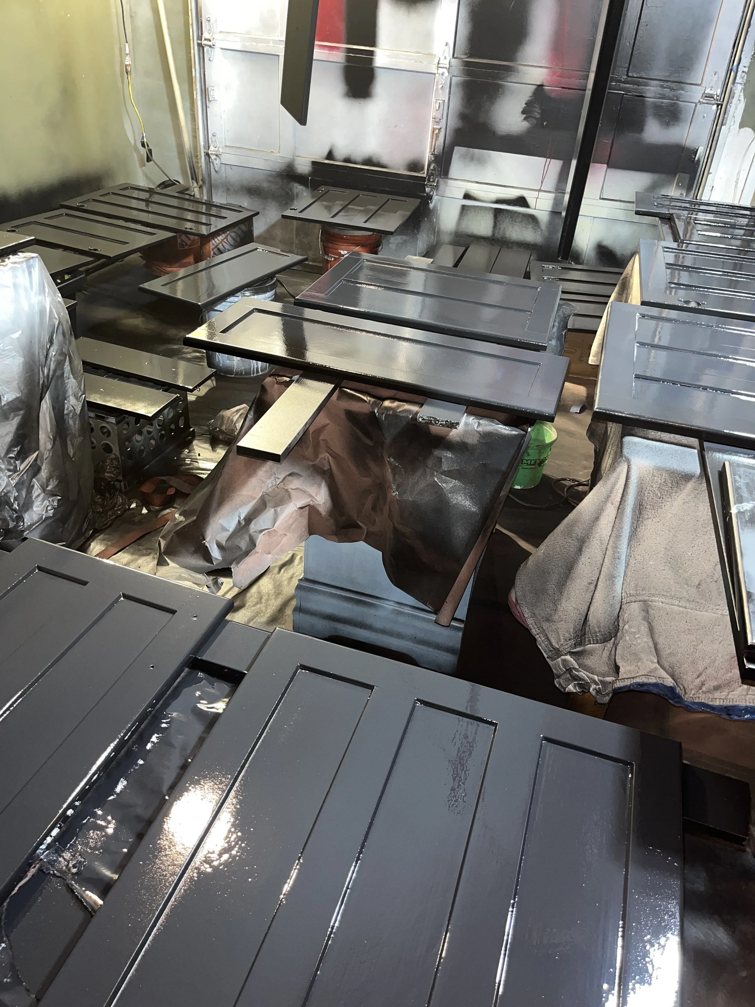 Multiple stainless steel kitchen cabinets and countertops in the process of being painted or coated, with some covered in brown paper and others freshly painted.