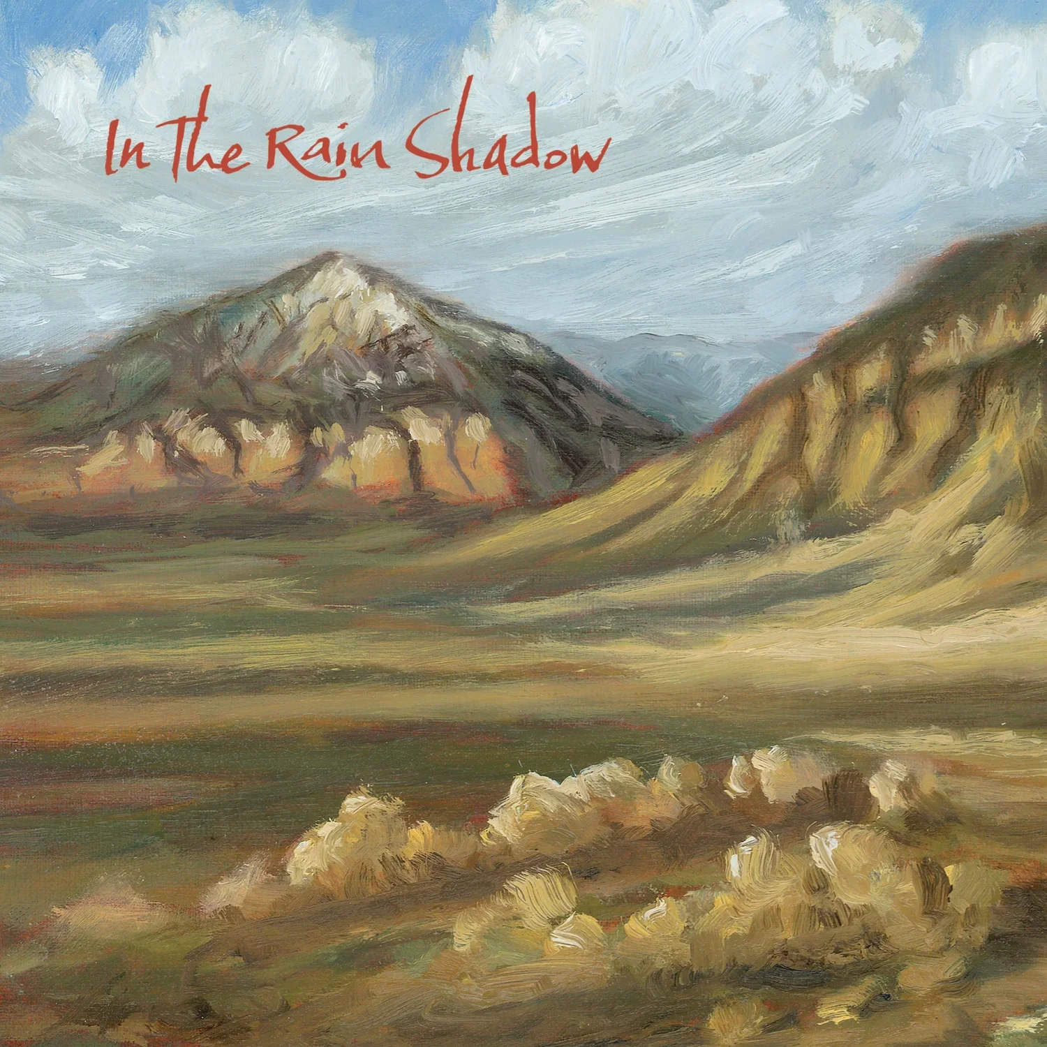 A landscape painting of mountains with a cloudy sky, grassy hills, and rocks in the foreground. The title "In the Rain Shadow" is written in red text at the top left.