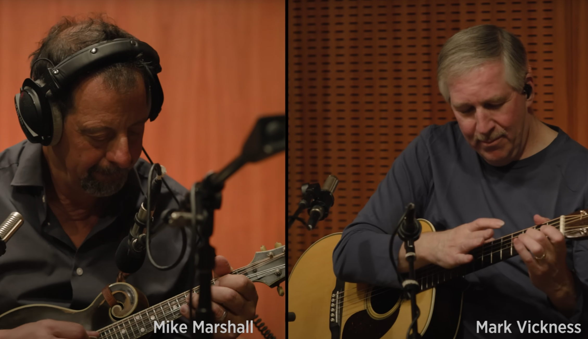 Two musicians playing guitars in a recording studio. The left musician, Mike Marshall, is wearing headphones and playing a mandolin, while the right musician, Mark Vickness, is playing an acoustic guitar. Both are focused on their instruments.