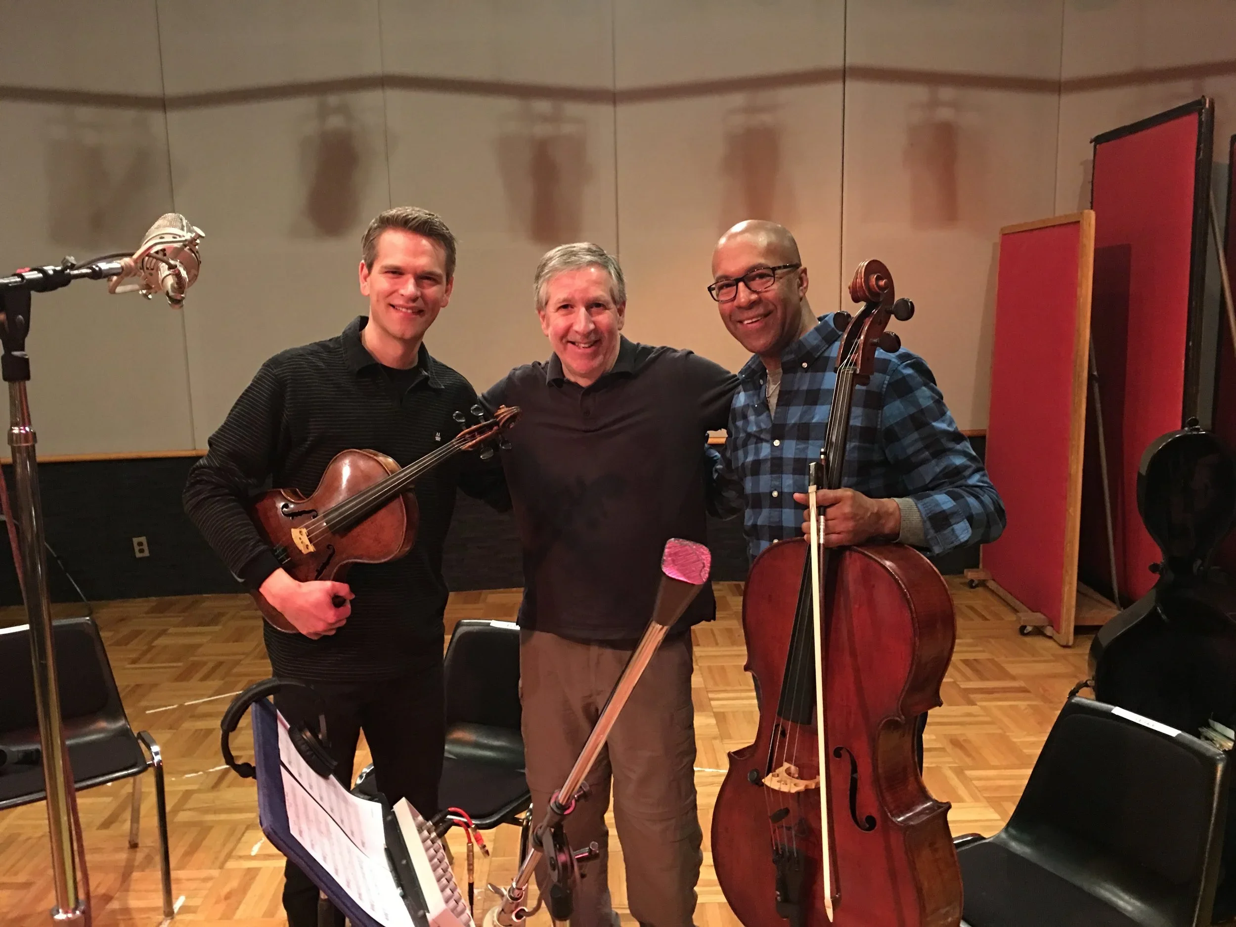 Mark Vickness, Mads Tolling, and Joseph Hebert. Three men in a music recording studio, two holding violins, smiling and standing close together.