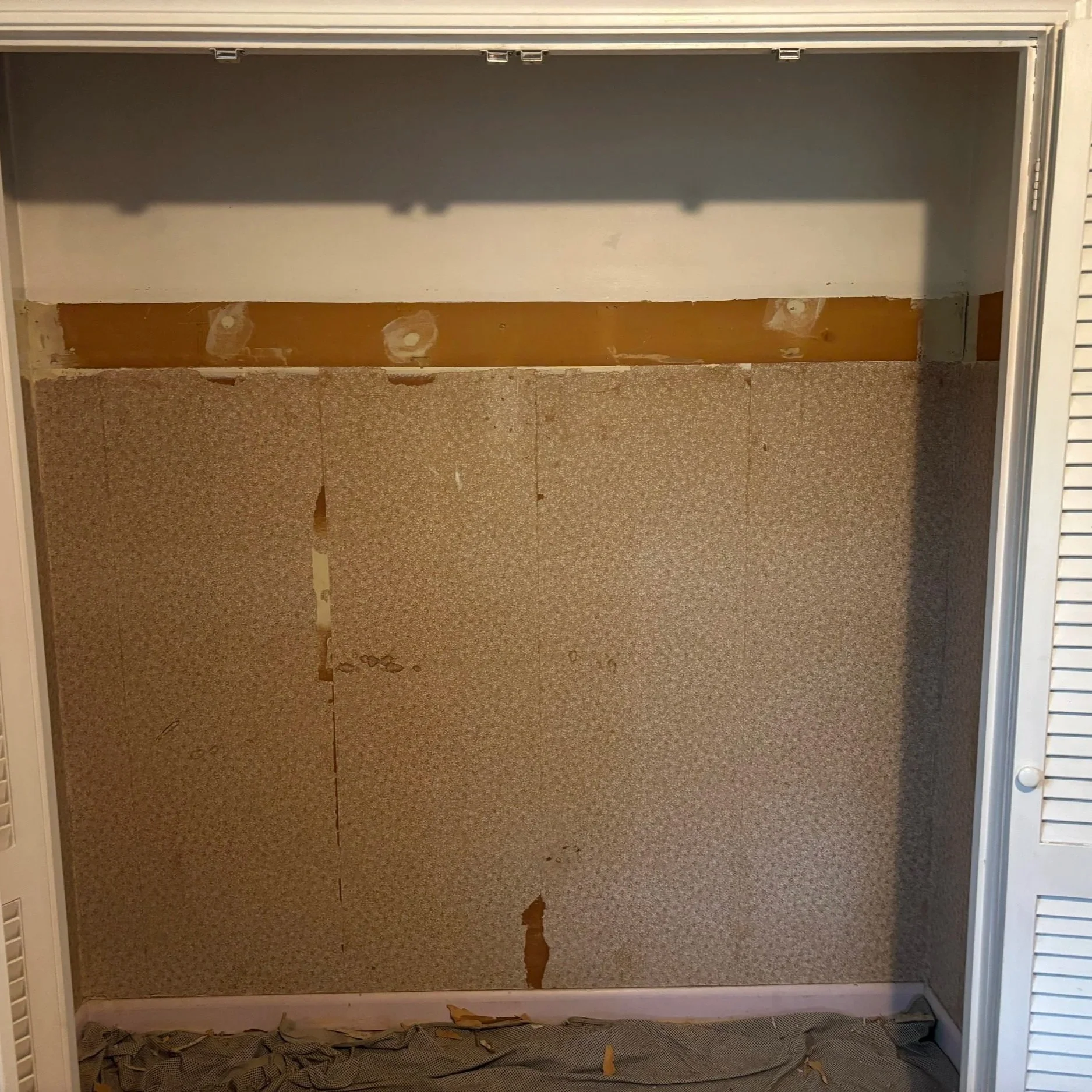 Empty closet with peeling wallpaper, open sliding doors, and exposed wall surface.