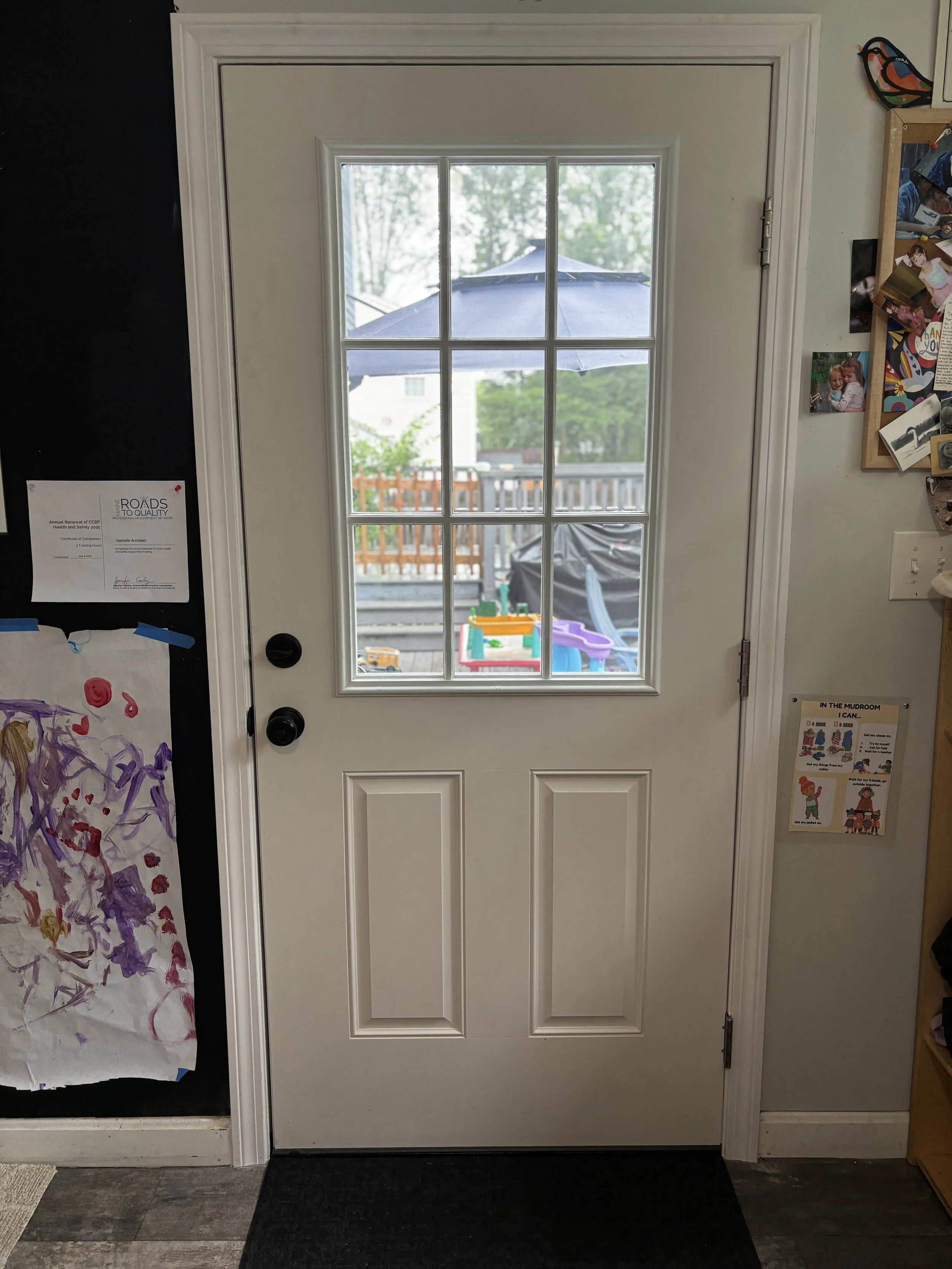 Exterior view of a door with a window, showing a backyard with a patio, a grill, a plastic slide, and a large umbrella outside.