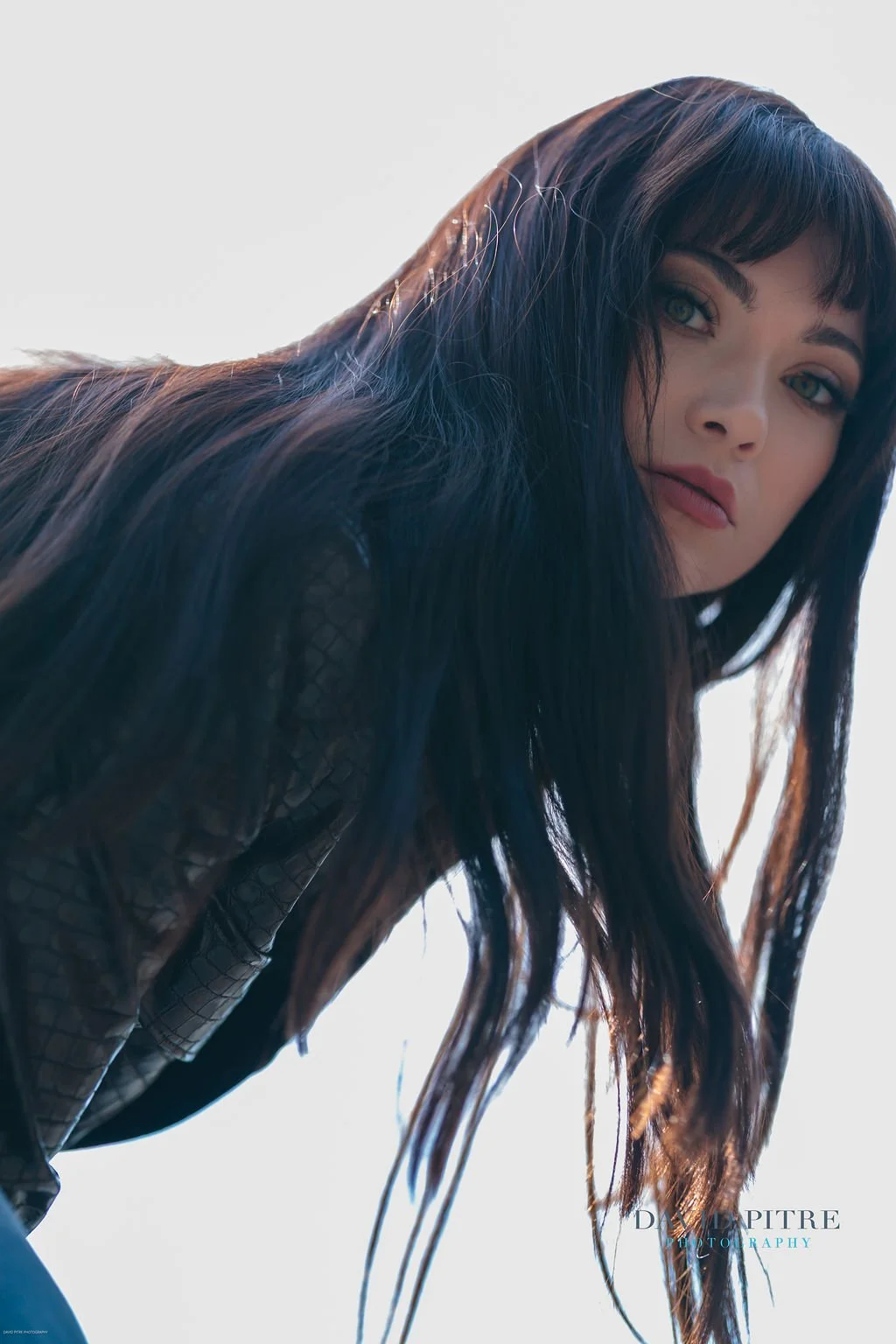 A woman with long, dark hair and green eyes looking at the camera against a plain background.