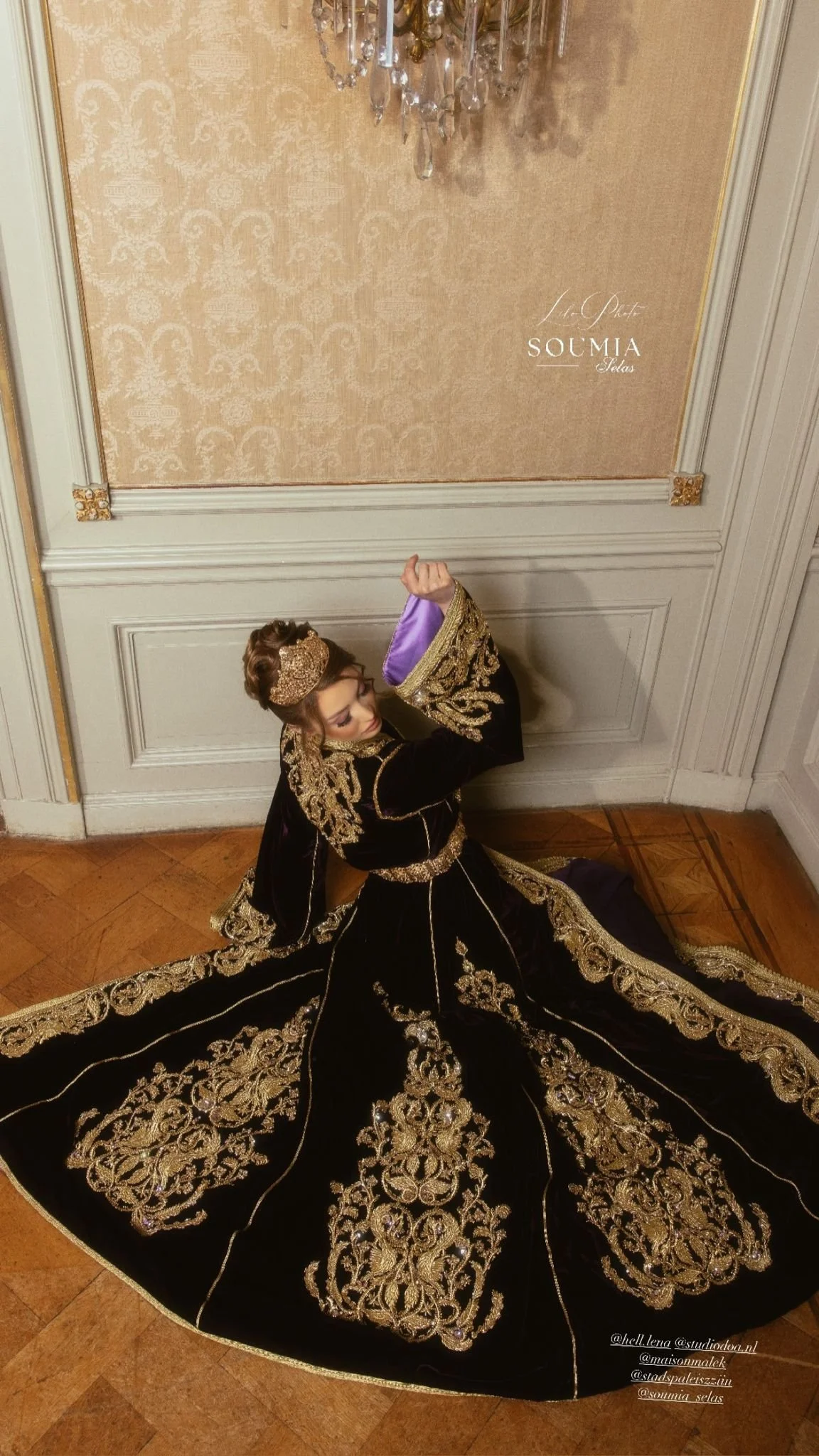 Vrouw in een zwart en goud versierd baljurk zittend op de vloer in een elegant interieur.