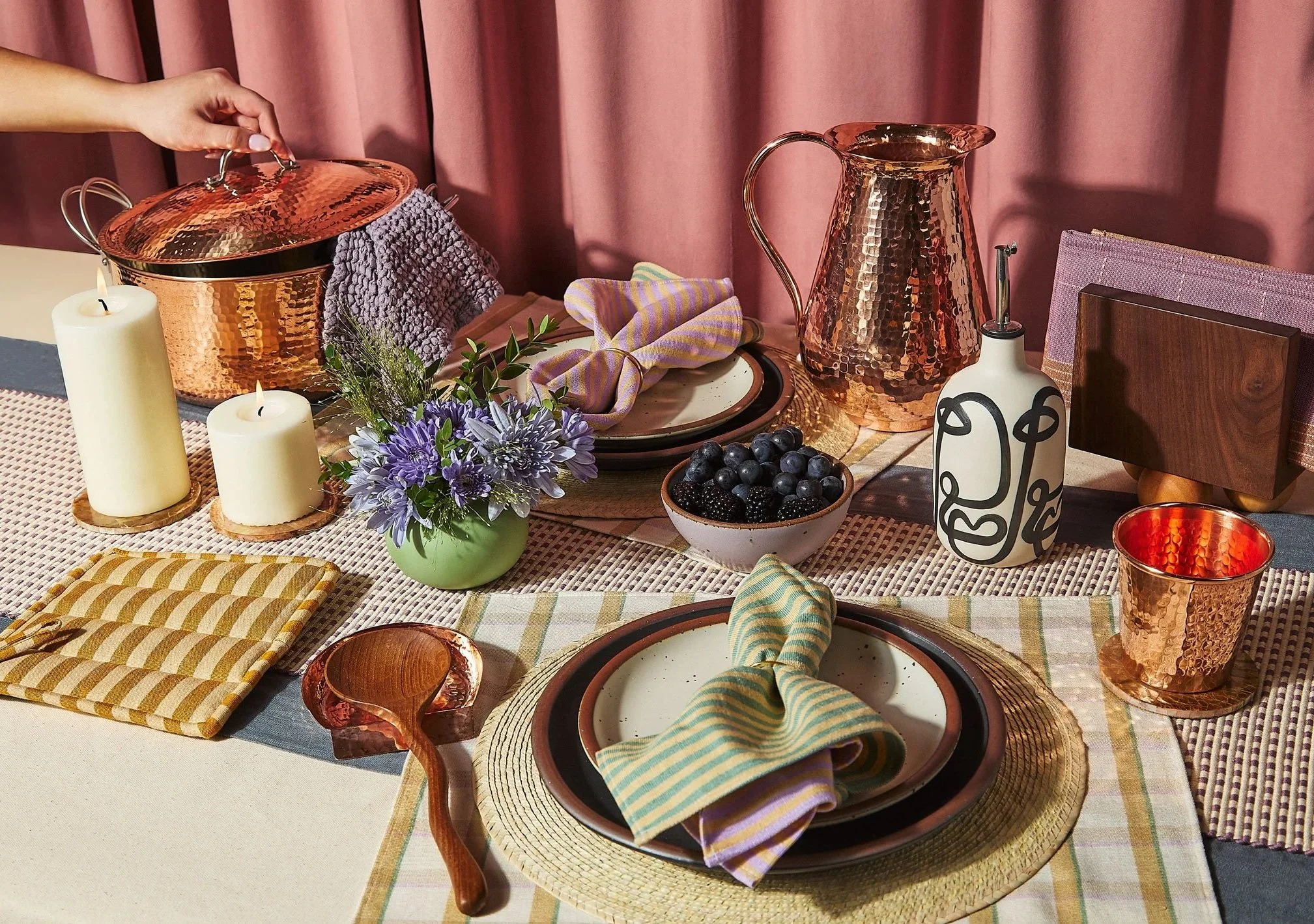 Custom Shopify Websites Service - A dining table set with pink and purple accents, including plates with striped napkins, a vase of purple flowers, candles, a bowl of berries, and copper and wooden tableware.