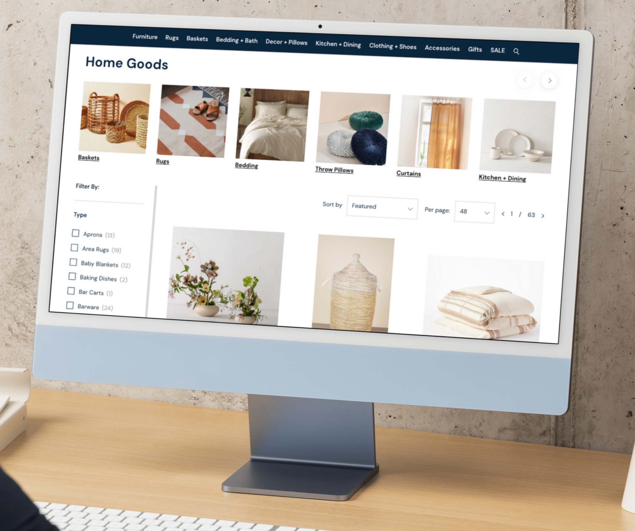 Computer screen displaying an online store's homepage for home goods, with categories like baskets, rugs, bedding, throw pillows, curtains, and kitchen plus dining, showing various product images.
