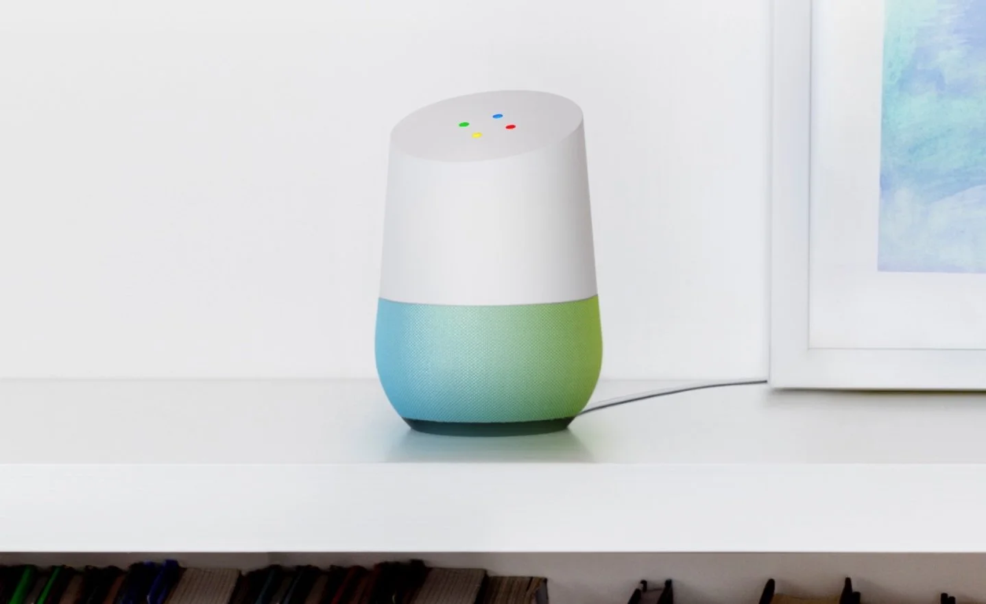 A Google Home smart speaker on a white surface, next to a framed photo.