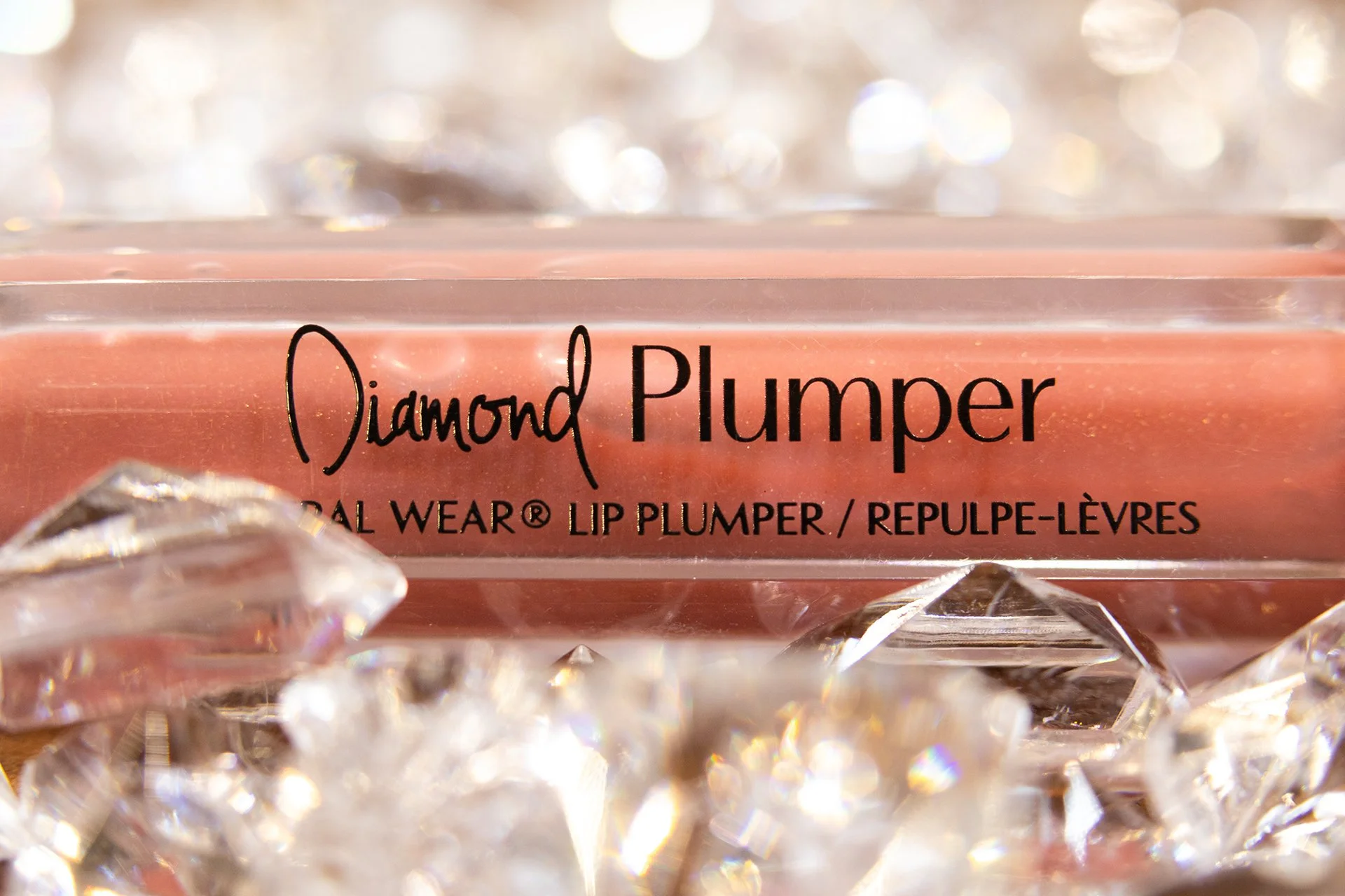 Close-up of a lip plumper product labeled 'Diamond Plumper' surrounded by clear, faceted crystals with a sparkling background.