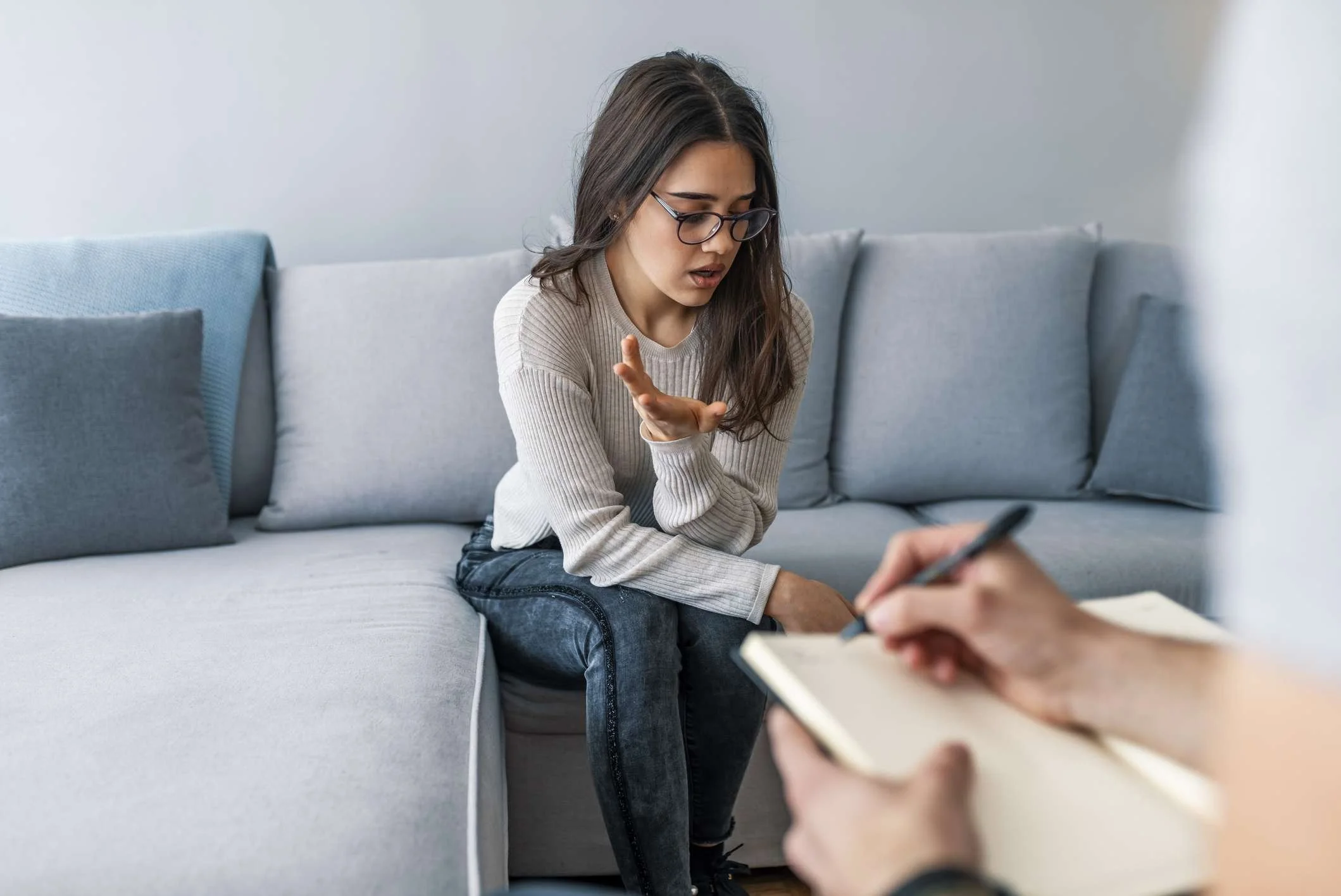 Therapist sitting on a sofa during a counselling session, speaking with a client who is taking notes in a calm, welcoming therapy space.