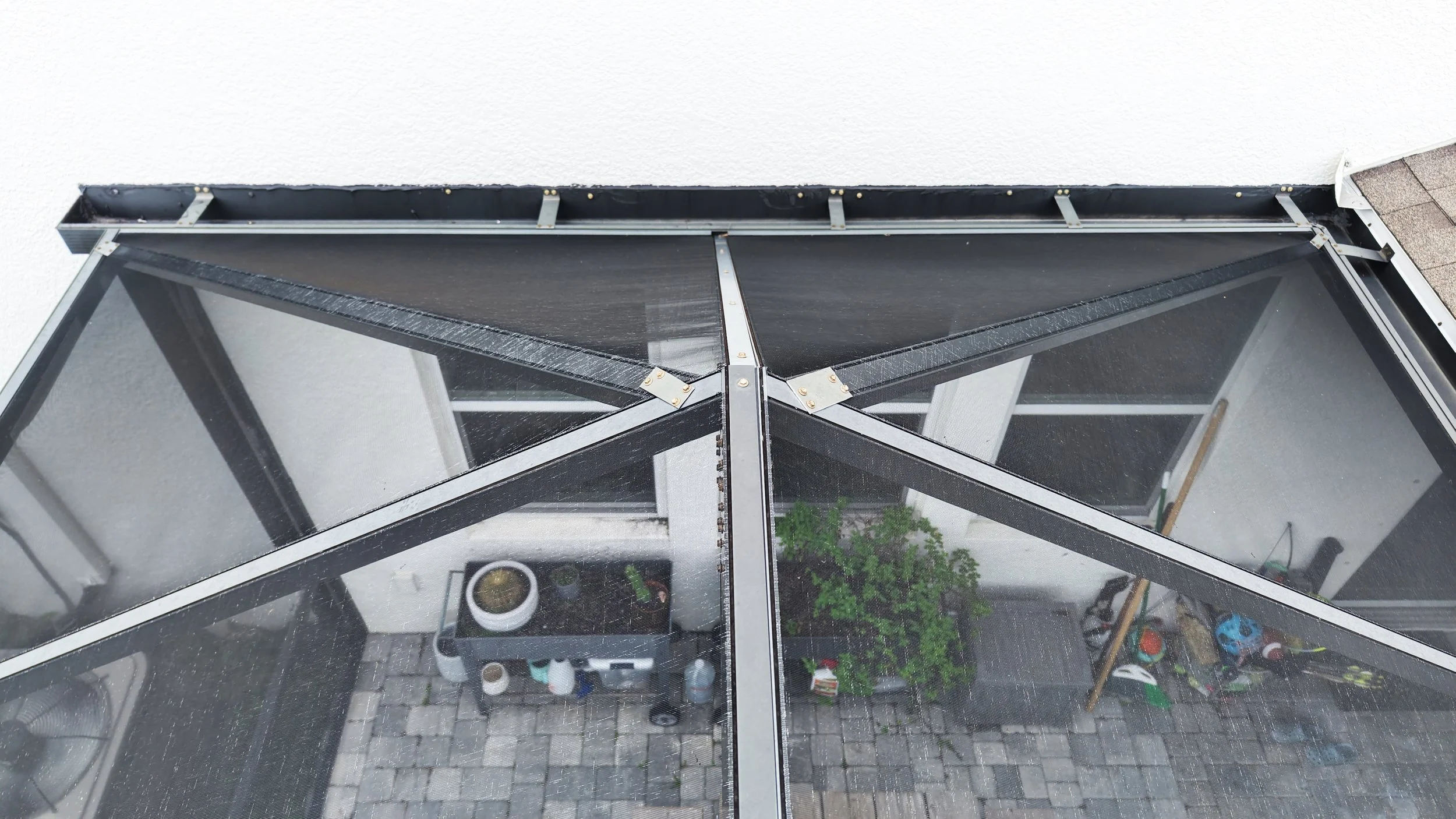 Top-down view of a screened porch with a black frame, building materials on the ground, and a potted plant inside.