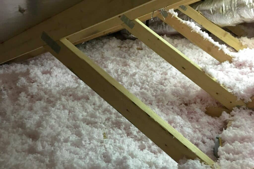 Insulation being installed in the attic space between wooden roof rafters.