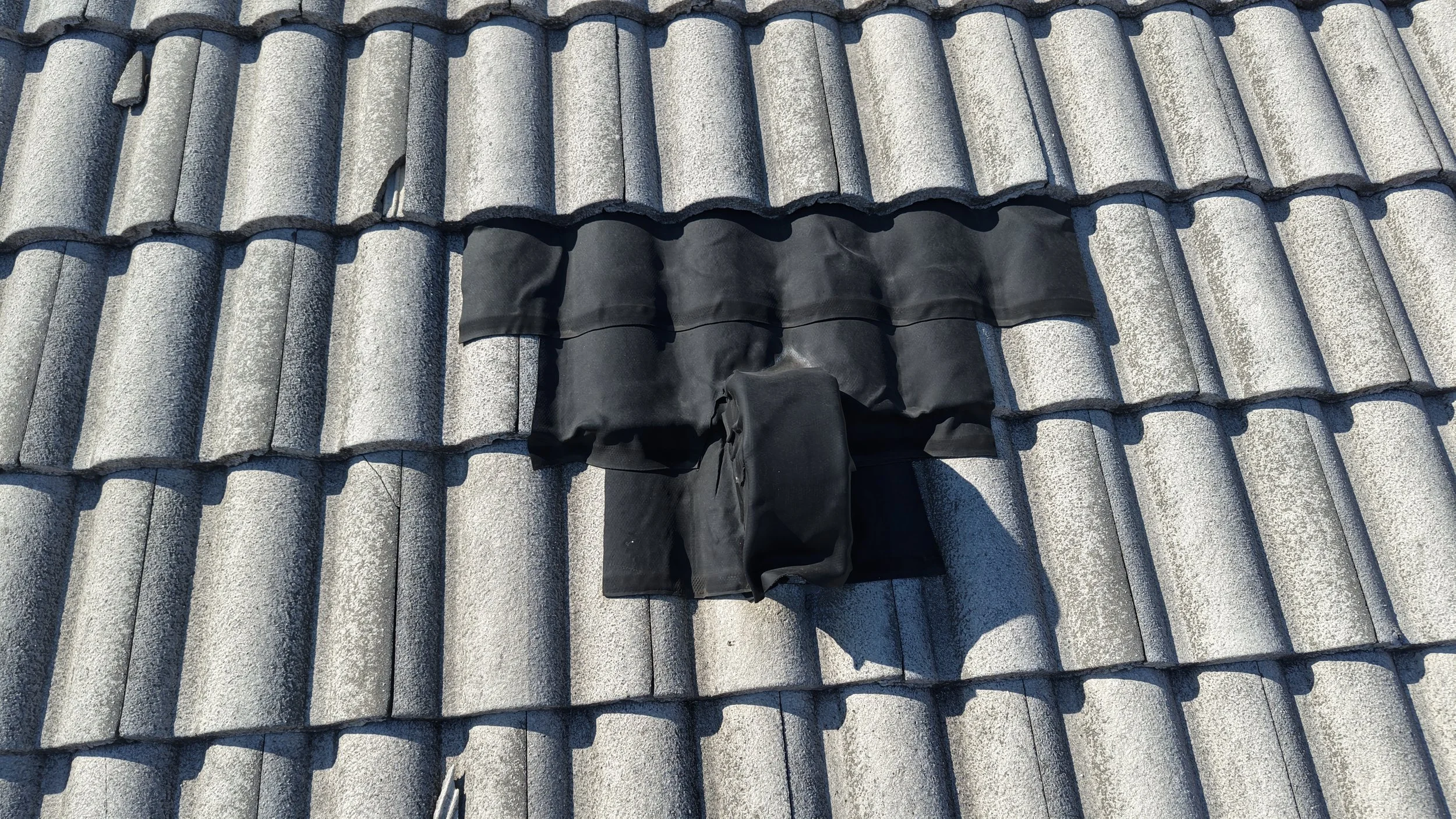 A black object, possibly a cover or tarp, partially draped over a hole in a gray tiled roof.
