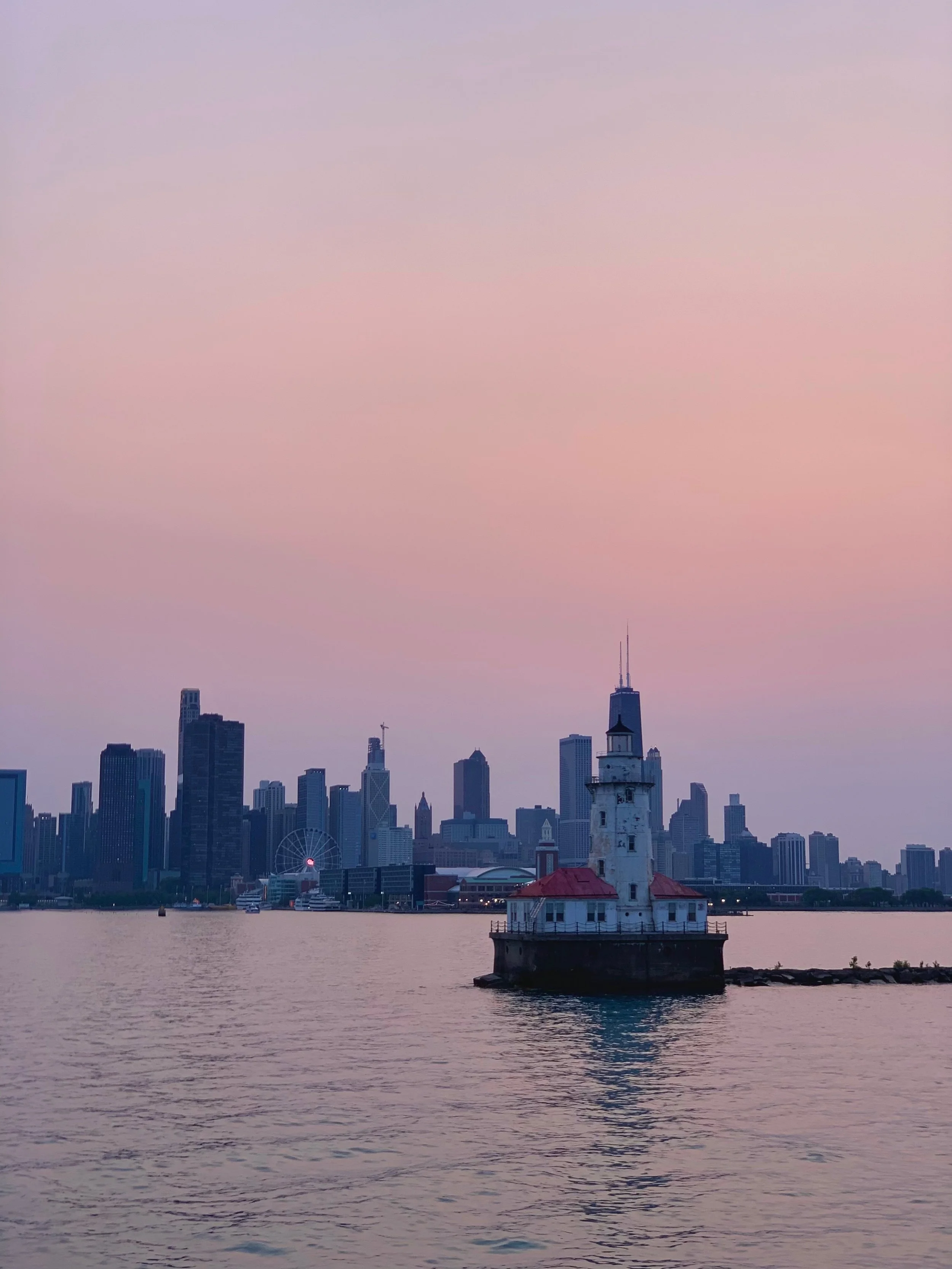 Lighthouse on a small island in a body of water with the Chicago skyline in the background at sunset or dawn.