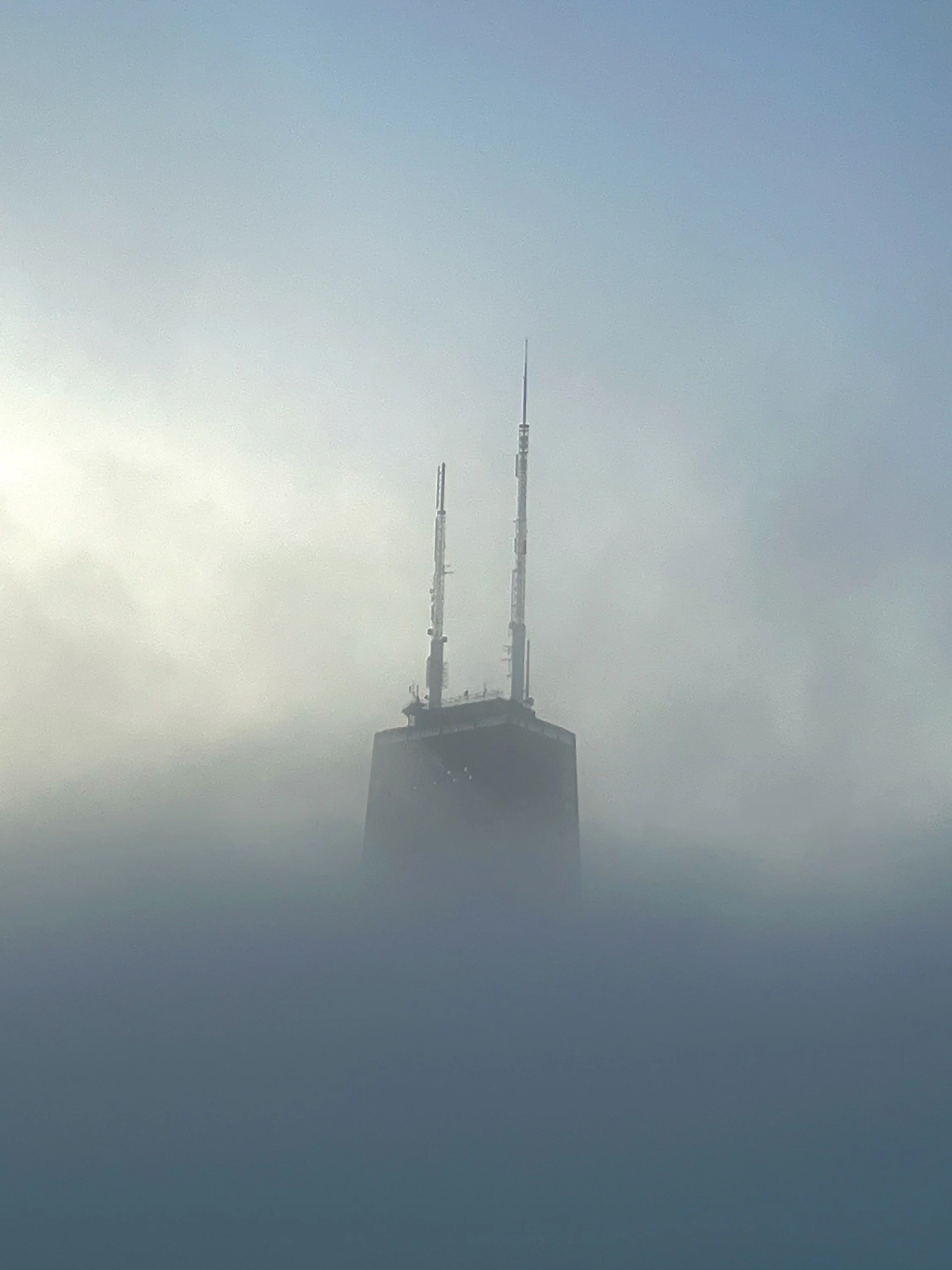 A tall building with antennas on top, partially obscured by fog or low clouds.