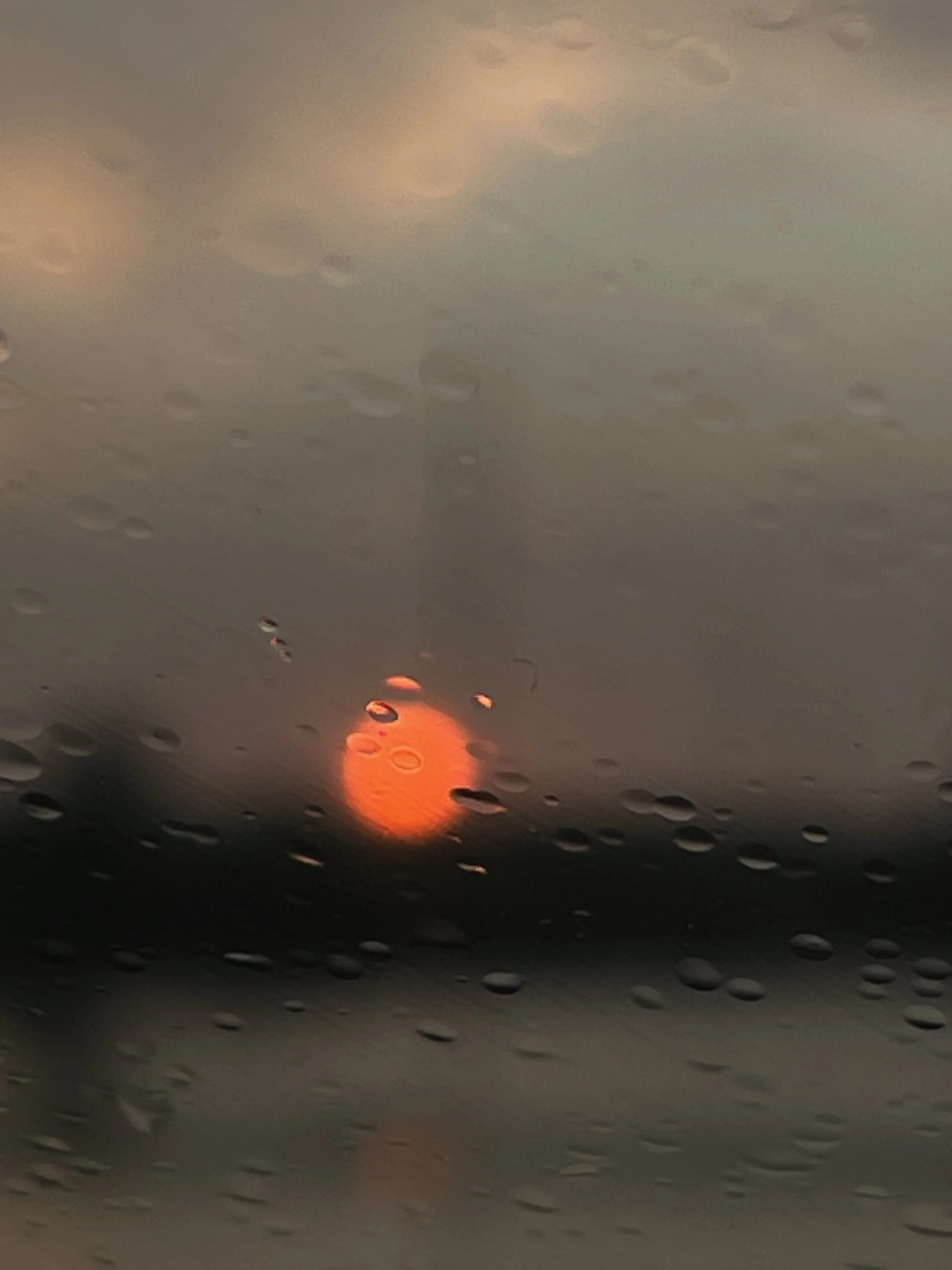 Raindrops on a car window with a blurred orange sunset and dark clouds in the background.