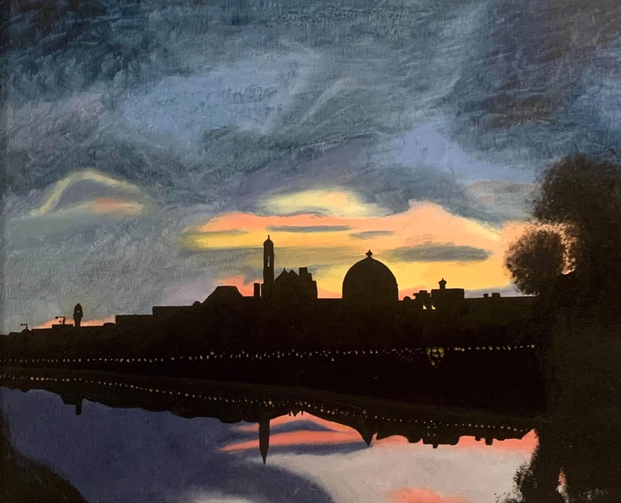 Silhouette of historic buildings and trees reflected on a river at sunset with colorful sky and dark clouds.