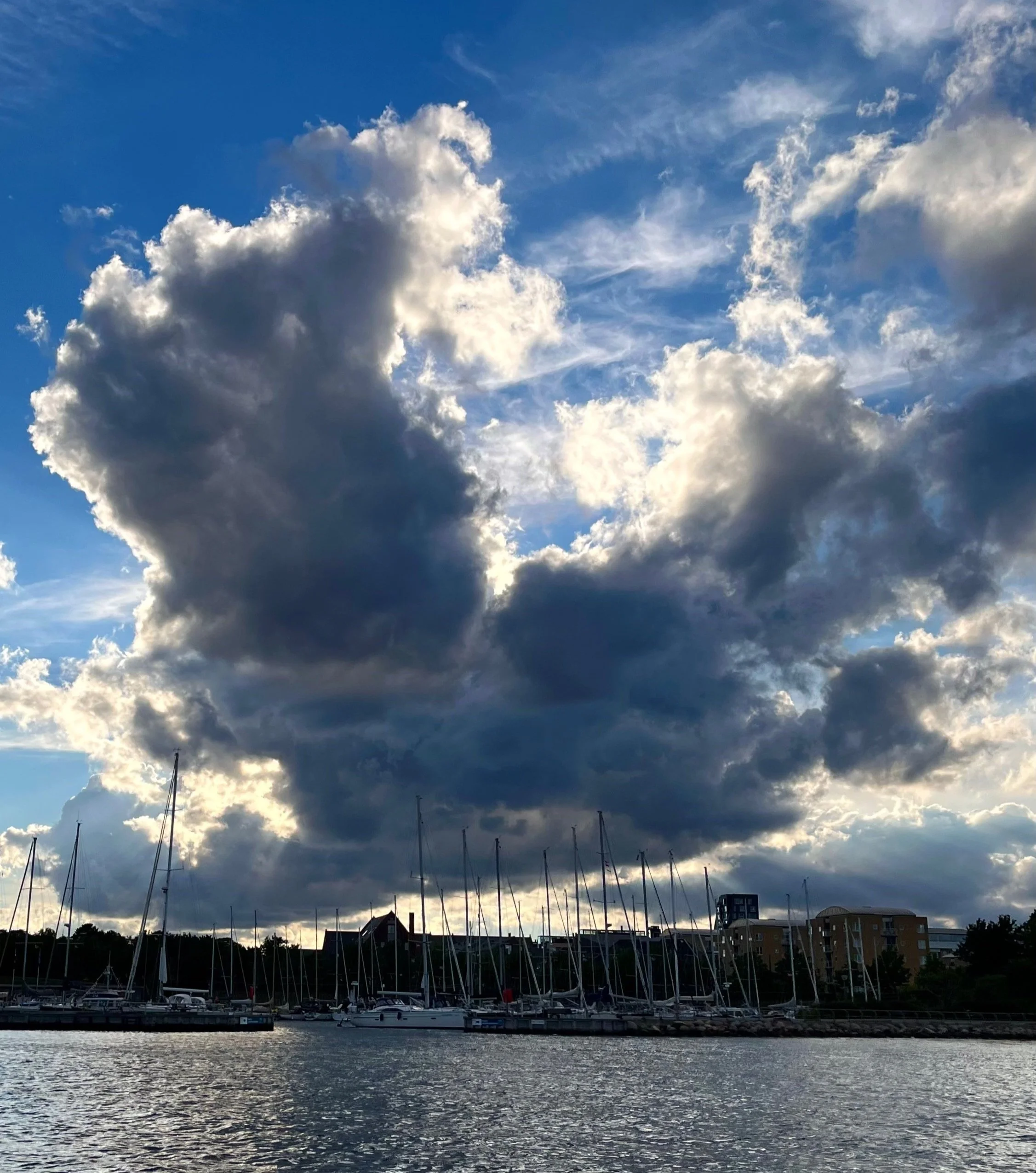 A harbor with sailboats on the water under a sky filled with large, dark and white clouds during the day. (copenhagen)