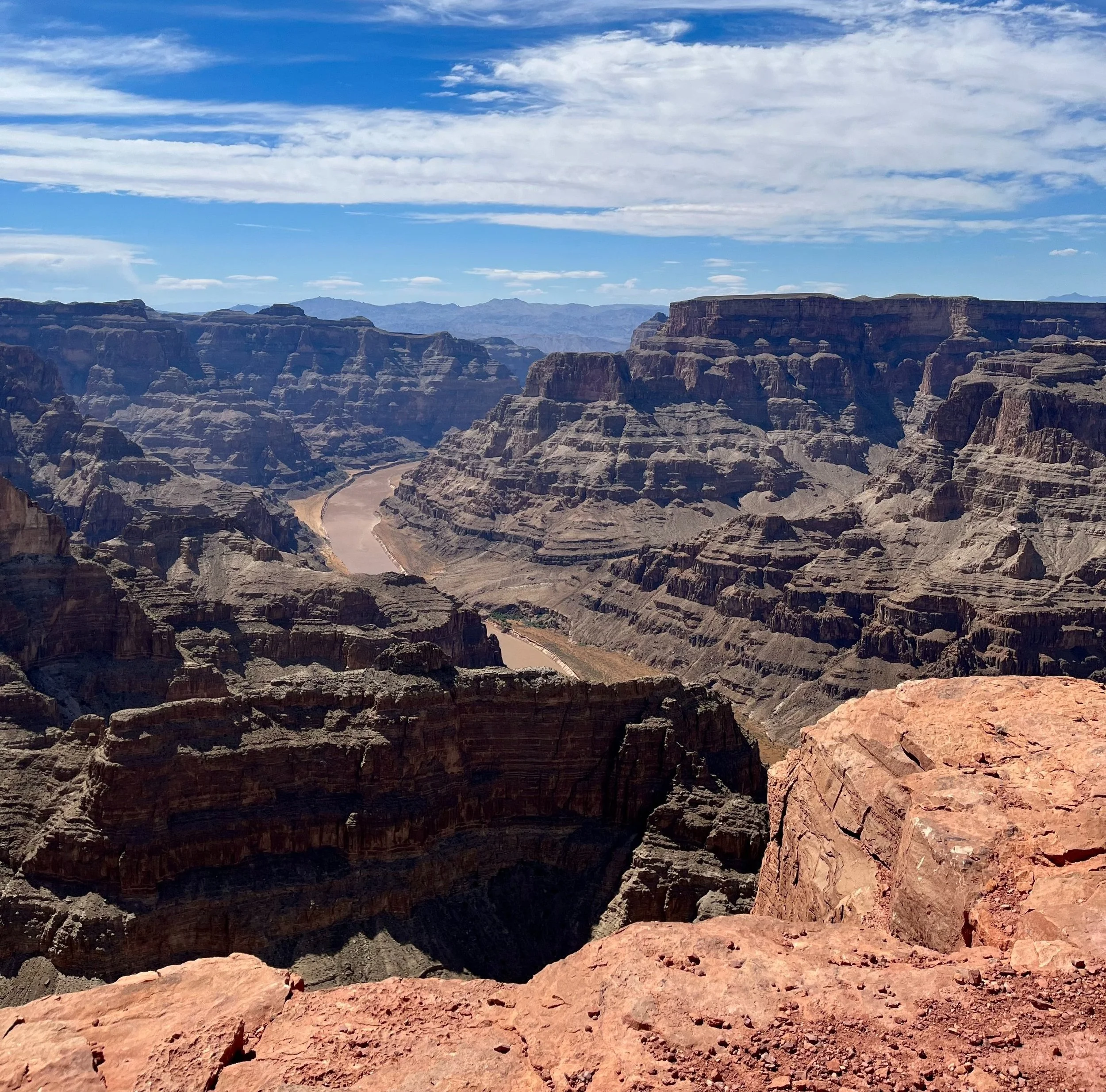View of the Grand Canyon with layered rock formations, a winding river at the bottom, and a partly cloudy sky.