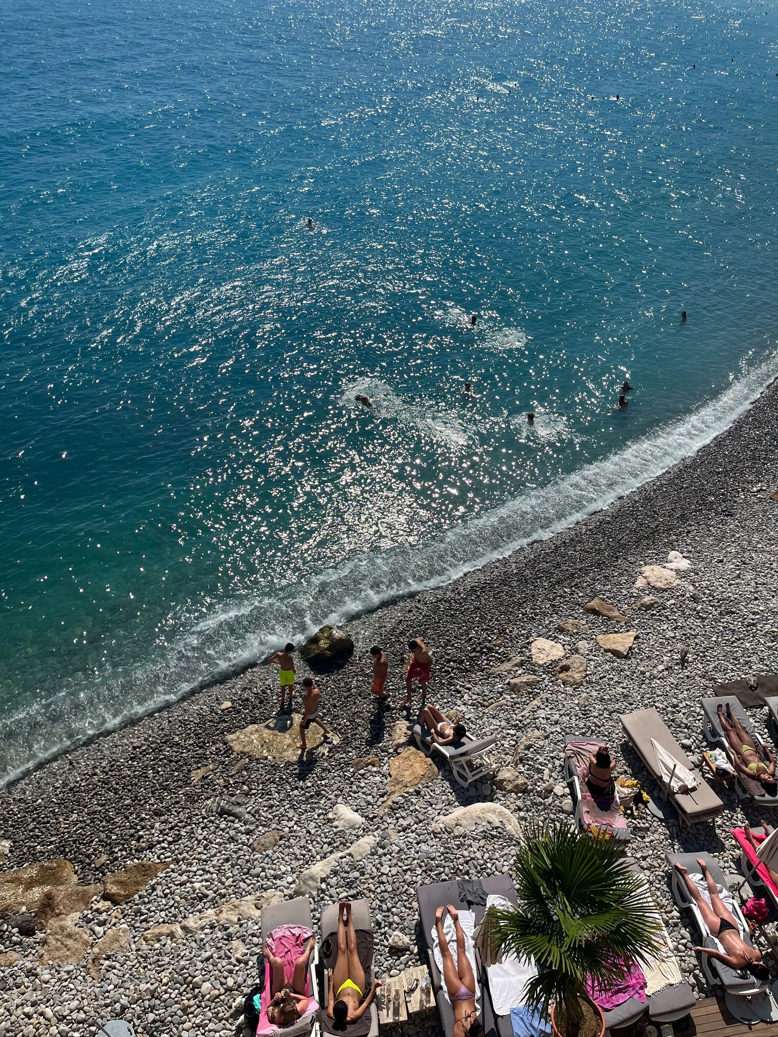 Beach scene with people sunbathing on lounge chairs and swimming in the ocean (nice, france).