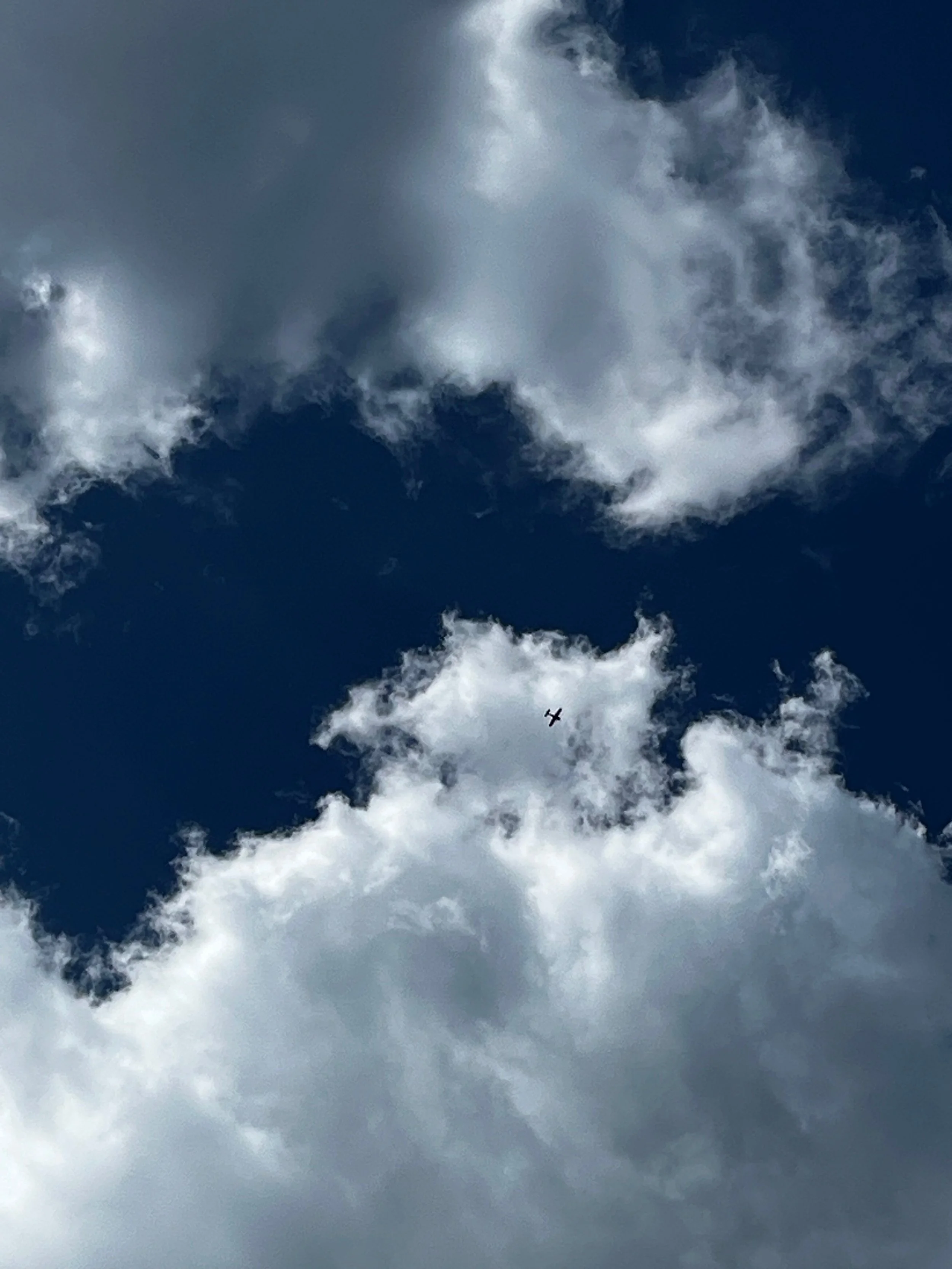 A small airplane flying through a sky with large, fluffy clouds.