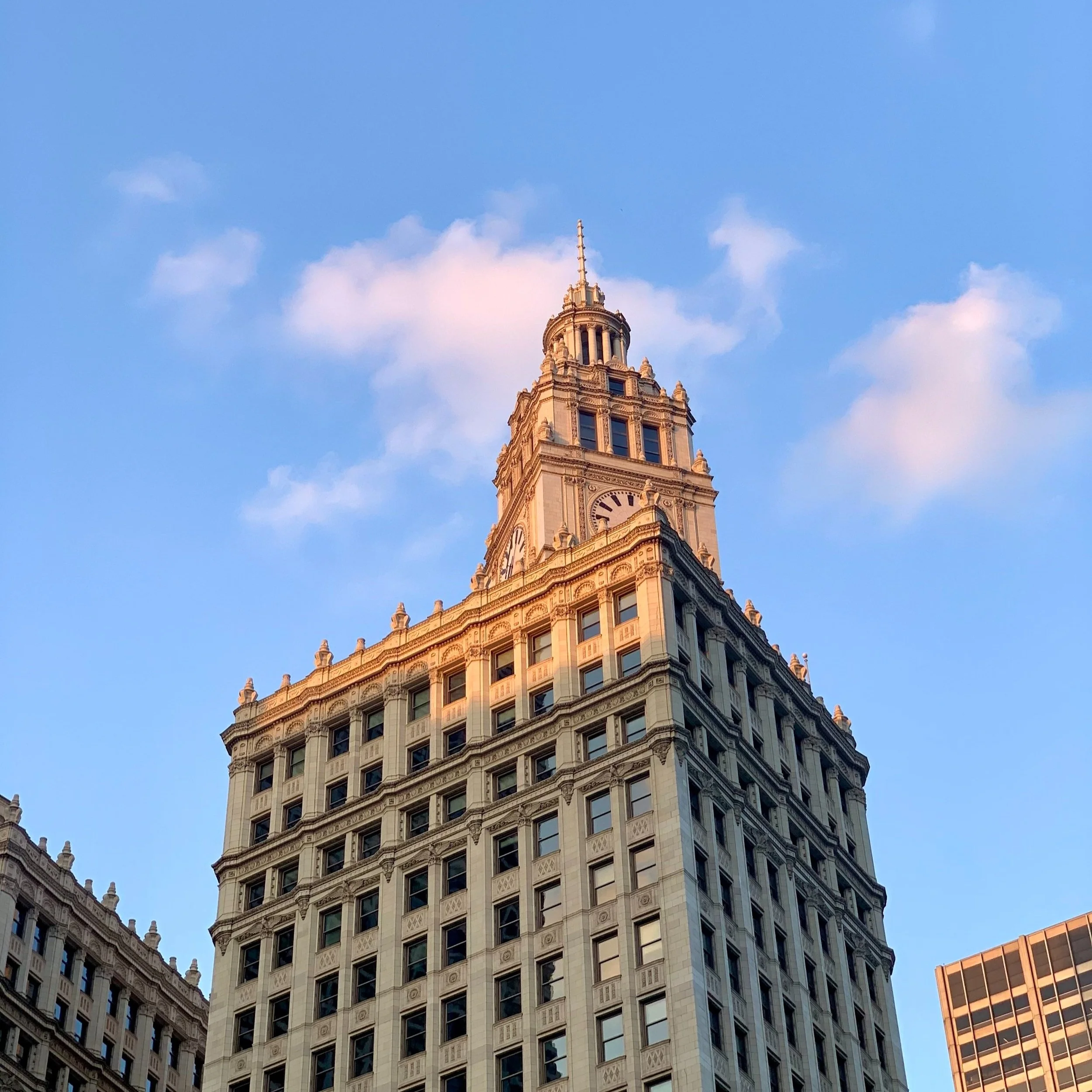 Tall historic building with a clock and spire against a blue sky with clouds. chicago, wrigley building
