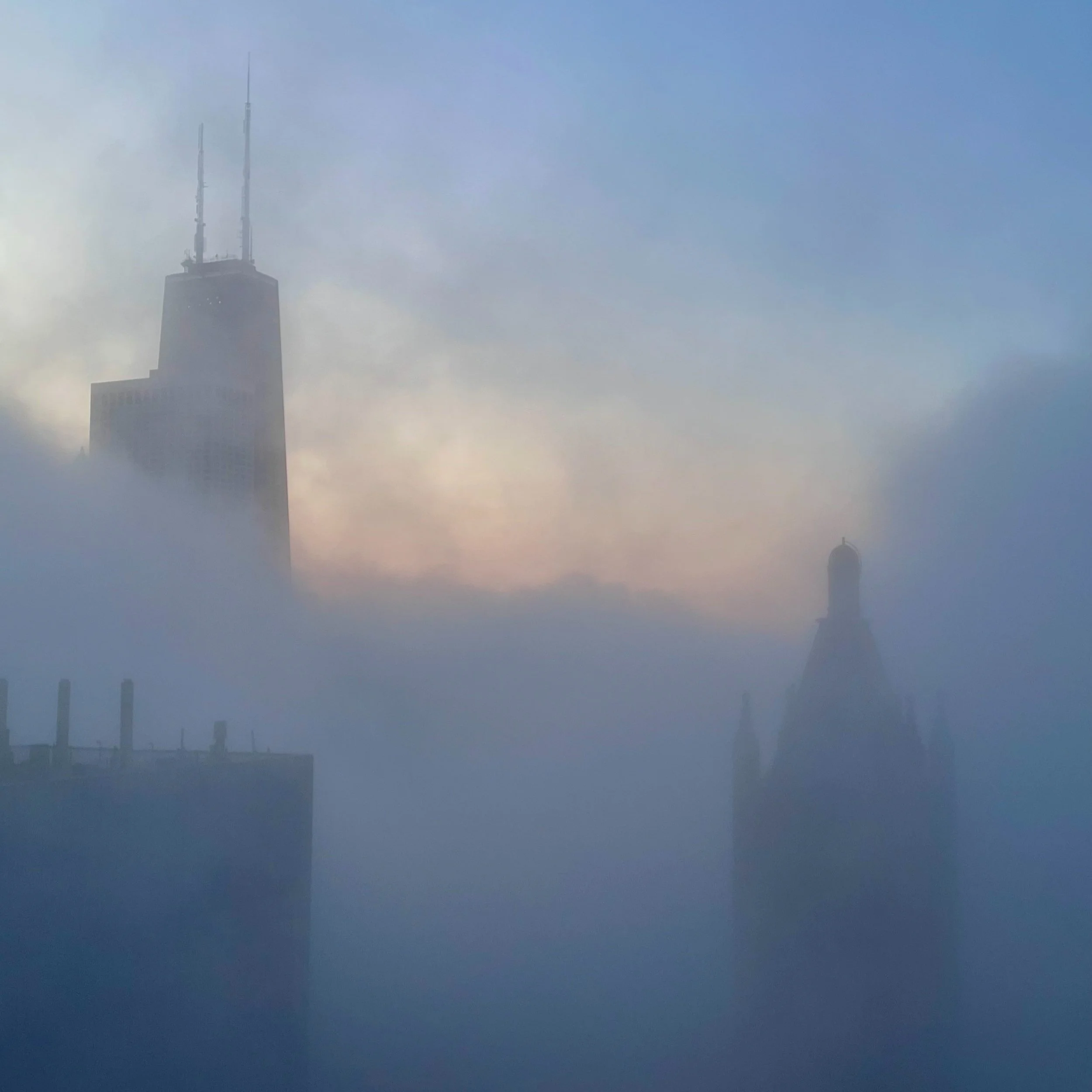 Skyscrapers partially obscured by fog with a soft pastel sunrise or sunset in the background. chicago
