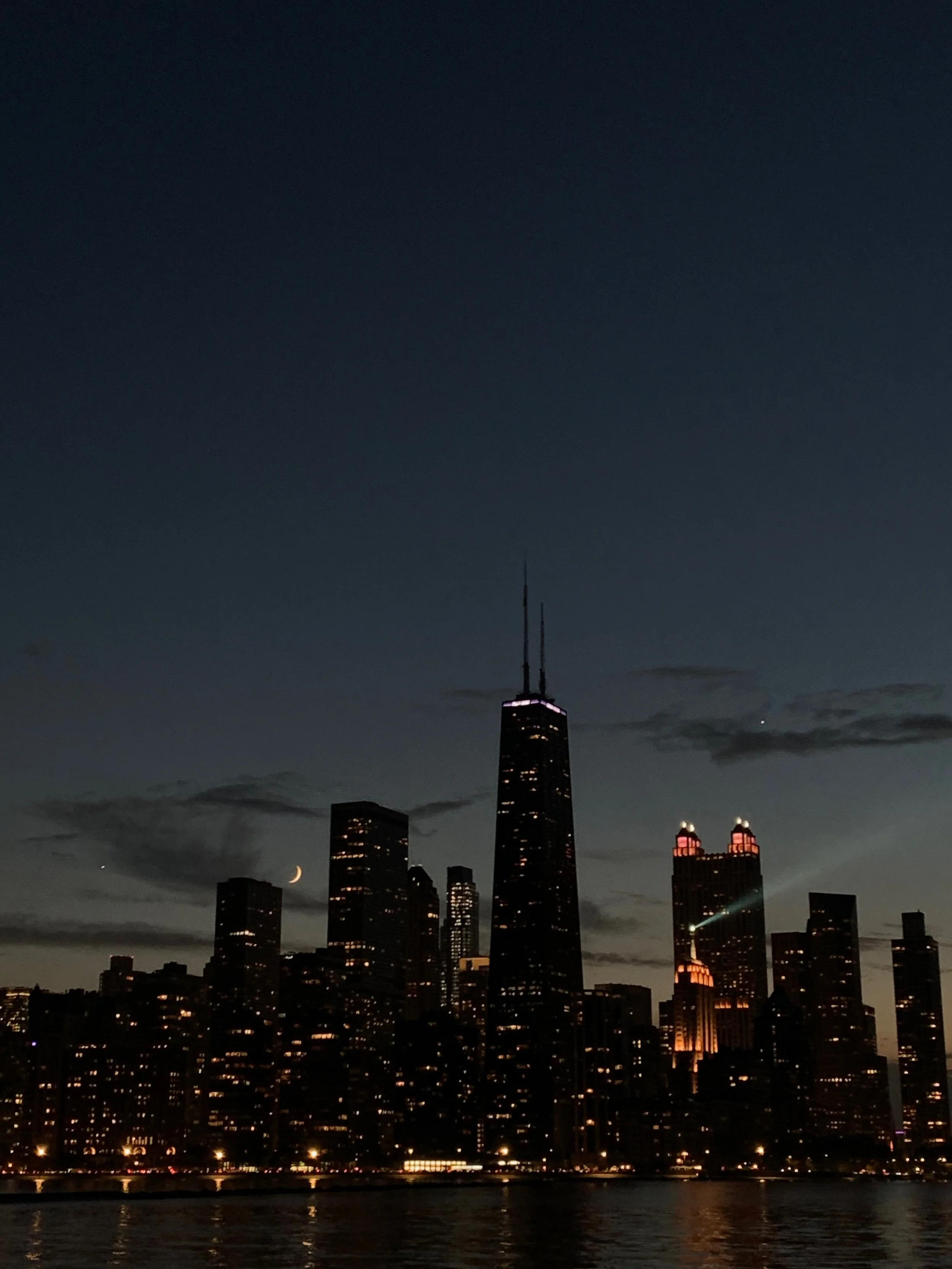 A crescent moon peeks through a slightly cloudy skyline just as night falls and the city lights up, chicago, lake michigan