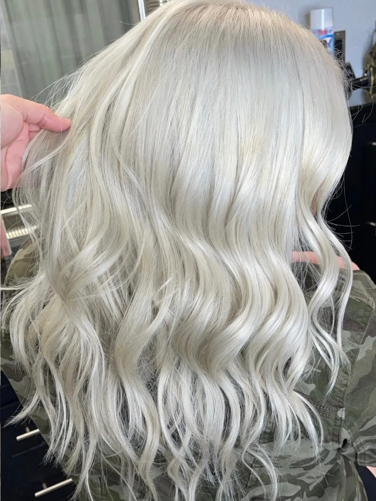 Back of a person with long, wavy platinum blonde hair, being styled in a hair salon.