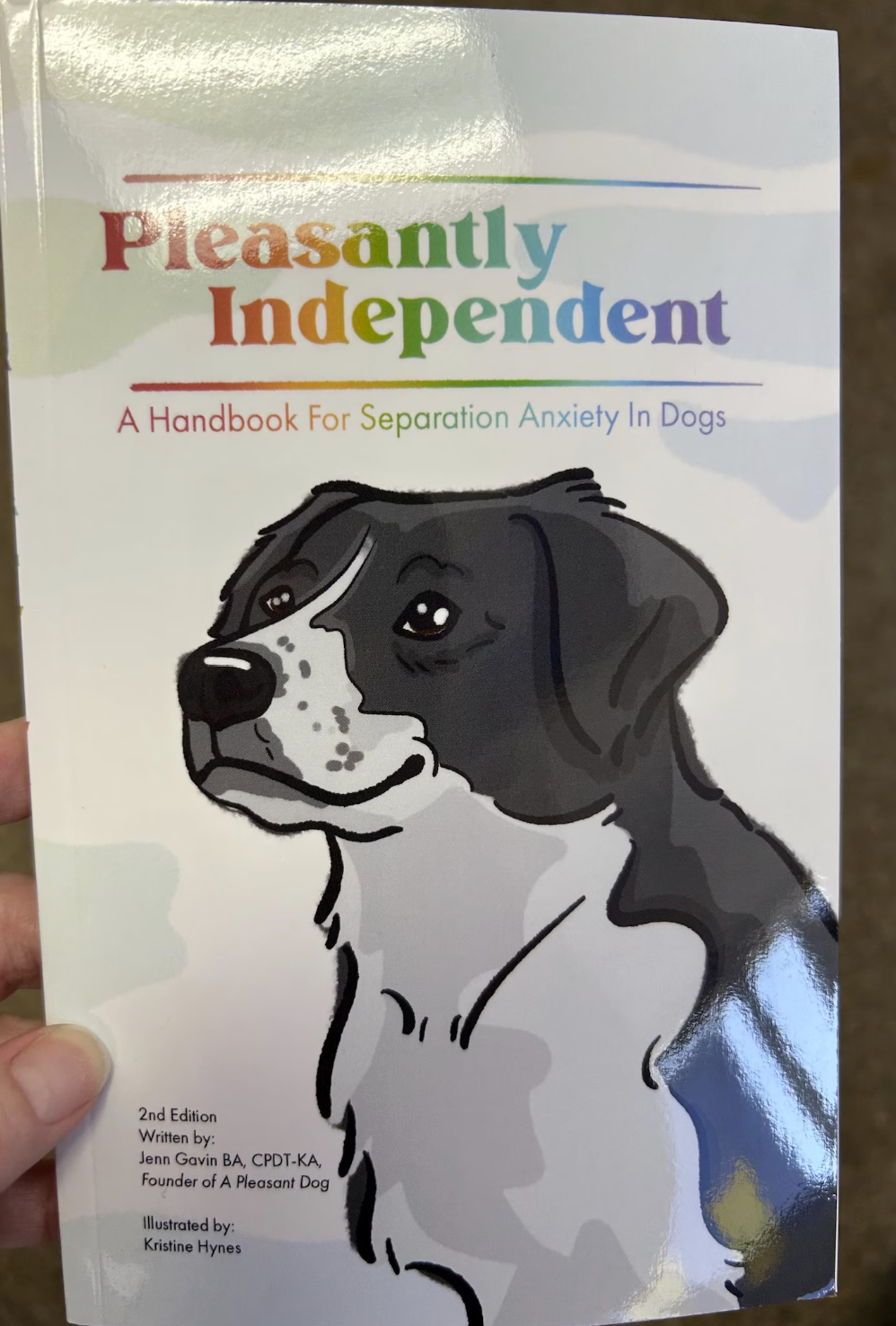 Book cover titled 'Pleasantly Independent: A Handbook For Separation Anxiety In Dogs,' featuring a cartoon illustration of a black and white dog with a calm expression.