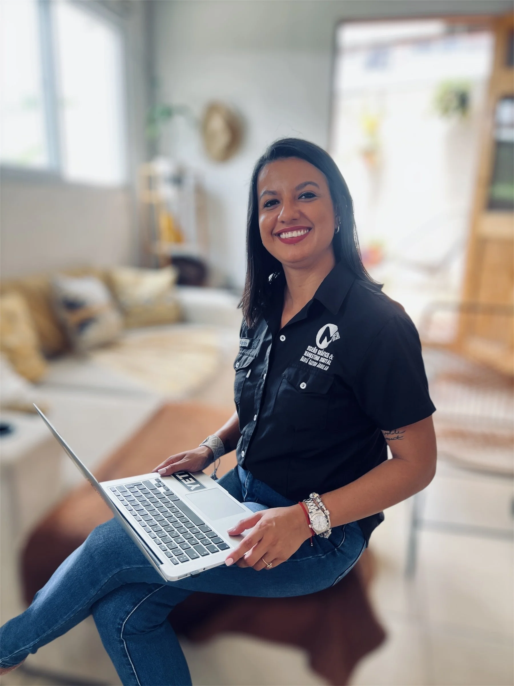 Mujer sonriendo, sentada en un mueble, con laptop en manos, en un ambiente interior moderno y bien iluminado.