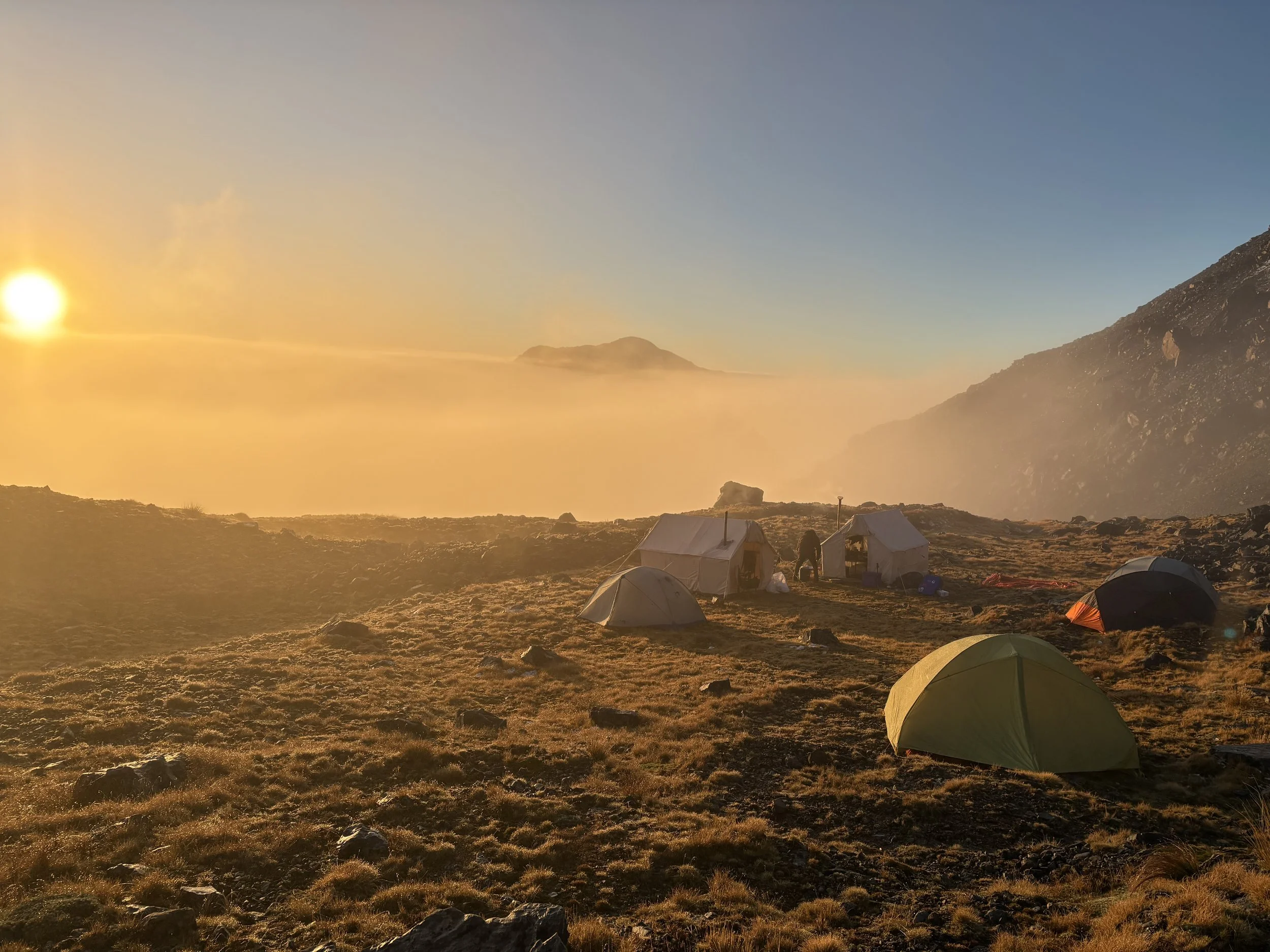 Tents set up on a mountain at sunrise, with fog and rocky terrain.