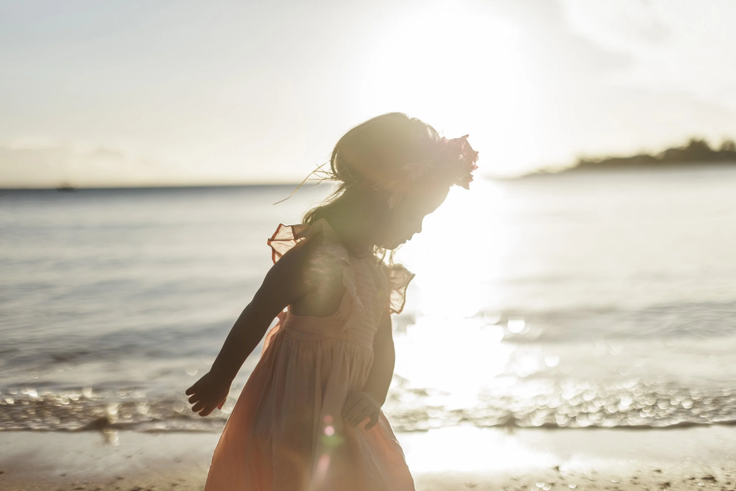 Une jeune fille portant une robe rose clair joue sur la plage au coucher du soleil.