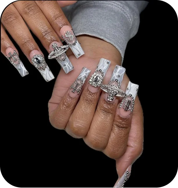 Close-up of hands with elaborate white and silver decorated acrylic nails and large silver jewelry, including rings and a bracelet.