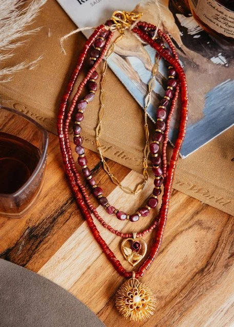 Three layered necklaces with red beads, gold accents, and a large gold heart with rose pendant