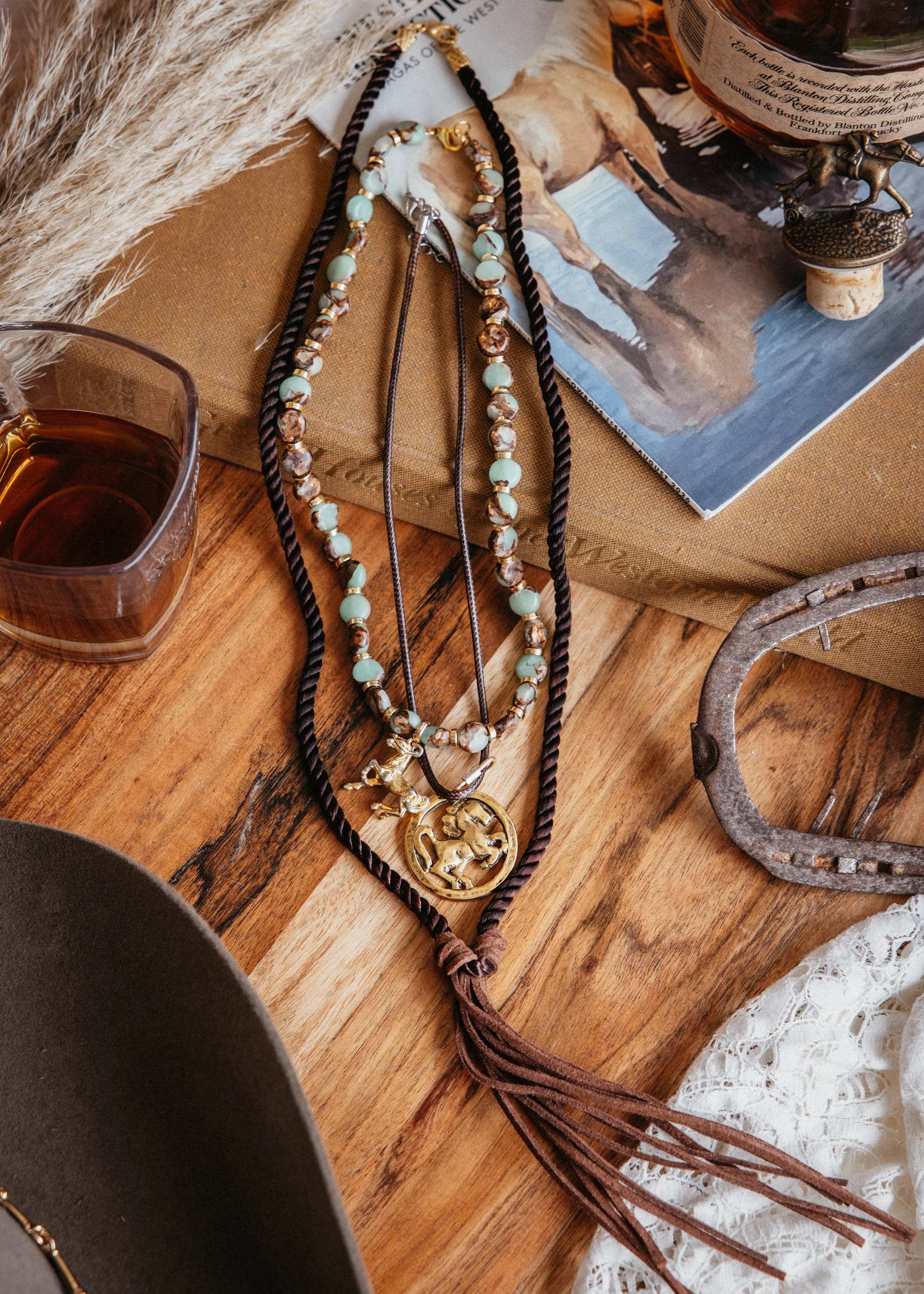 A collection of jewelry including a beaded necklace, a leather cord necklace, and a necklace with a horse pendant
