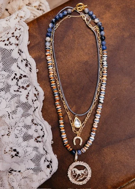 Three layered necklaces with beads, a pear-shaped pendant, a horseshoe charm, and a round pendant with a horse