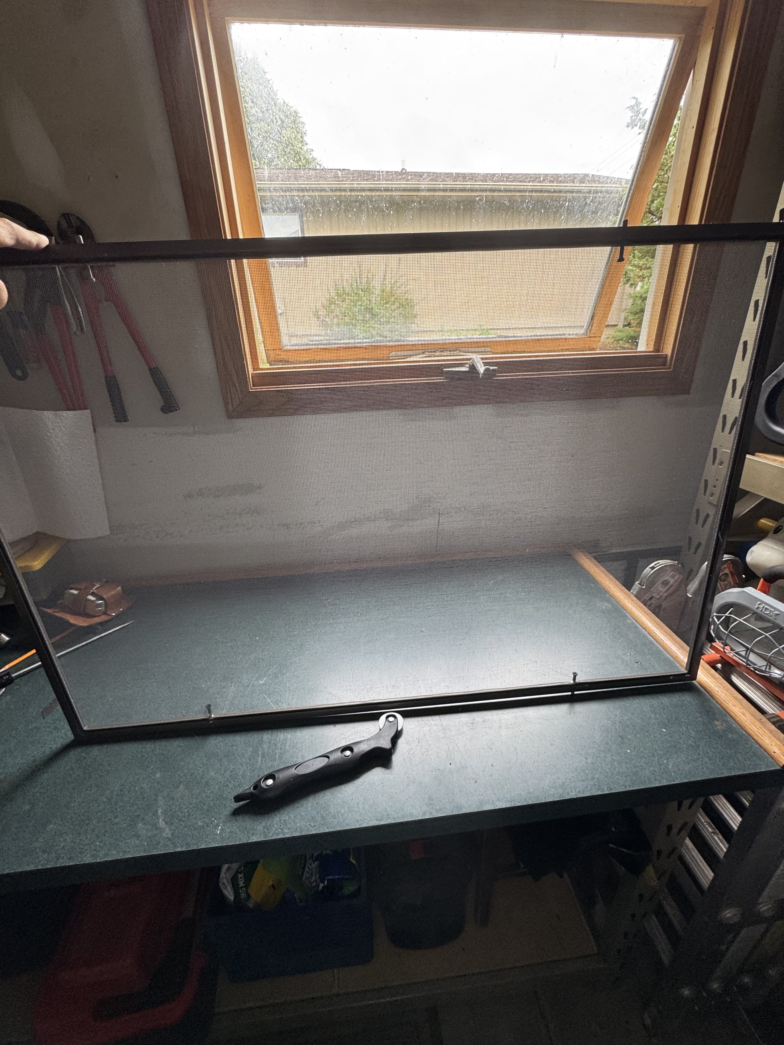 An empty insect screen or window screen frame on a work table inside a workshop with a window in the background.