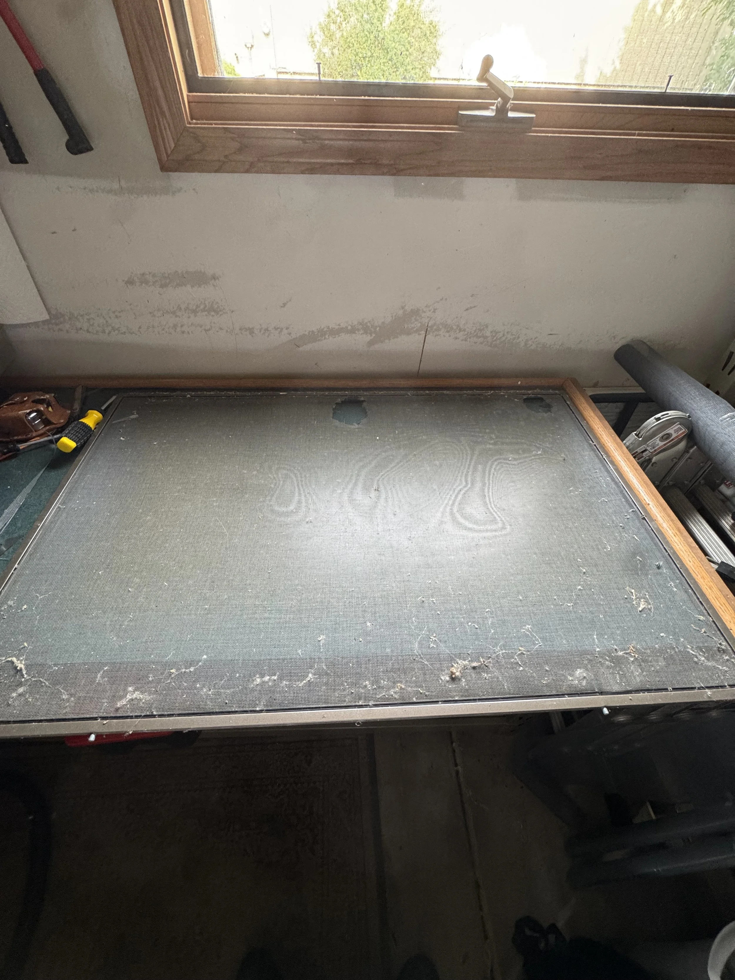 Dusty work table with sawdust and debris, positioned in front of a window with a wooden frame and a latch.
