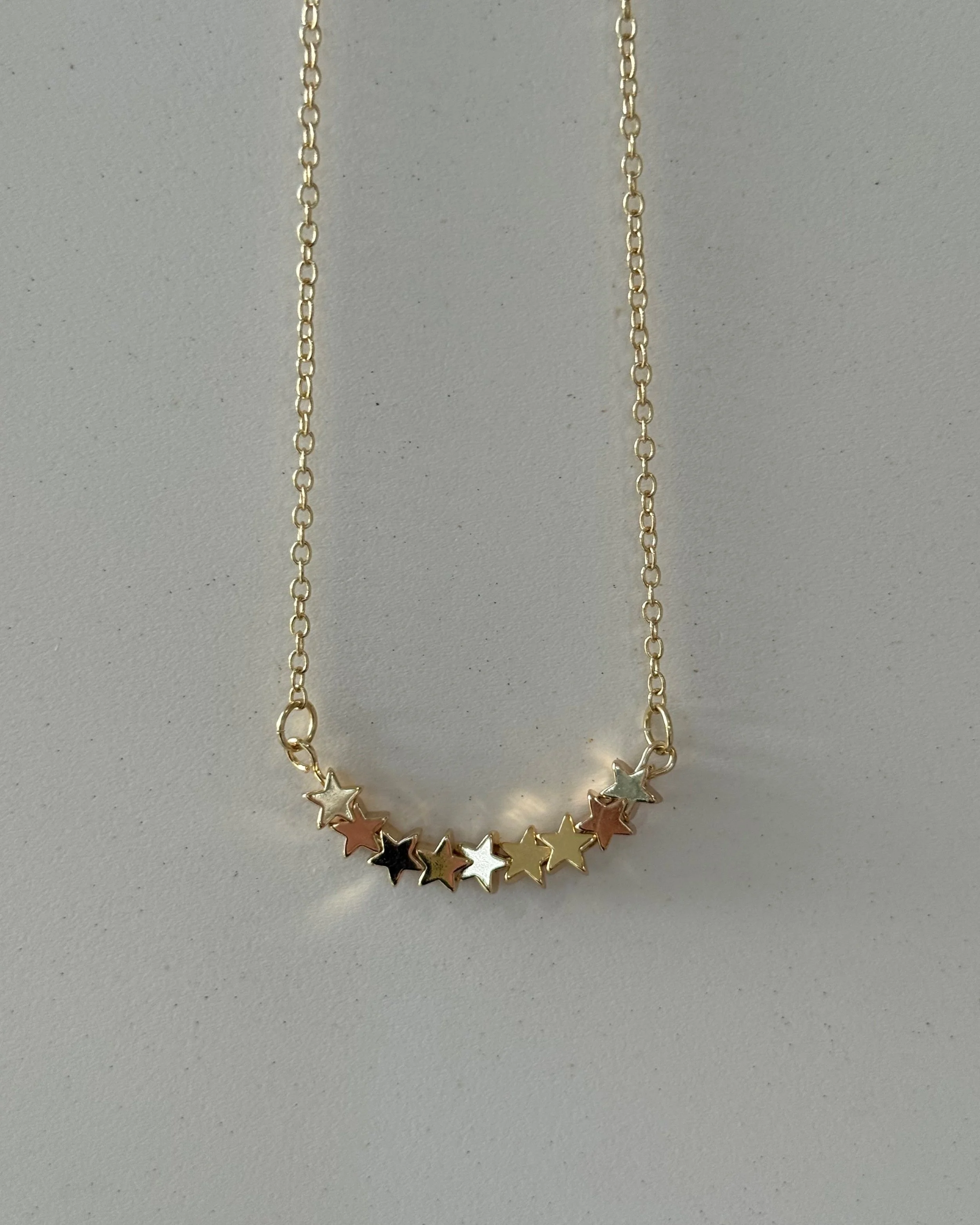 Gold chain necklace with a row of small, multicolored star-shaped pendants.