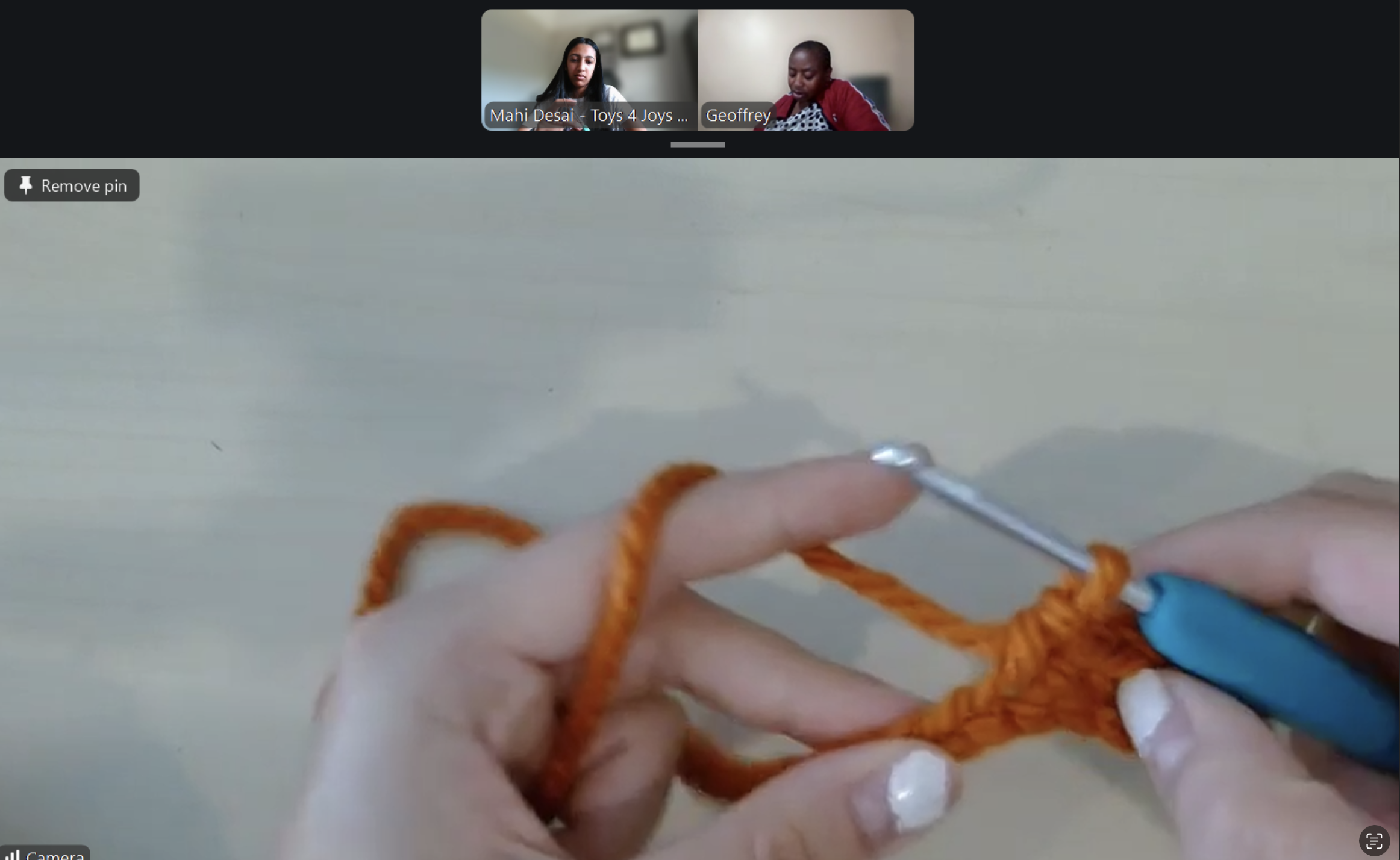 A person using knitting needles to knit with orange yarn.