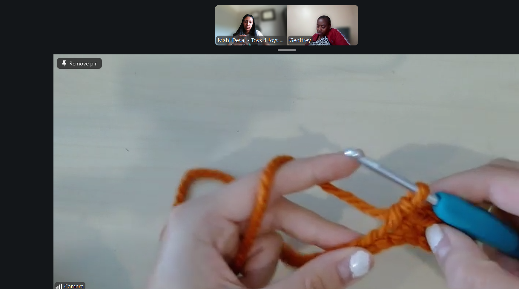 Close-up of hands crocheting with orange yarn, using a crochet hook, on a light-colored surface.