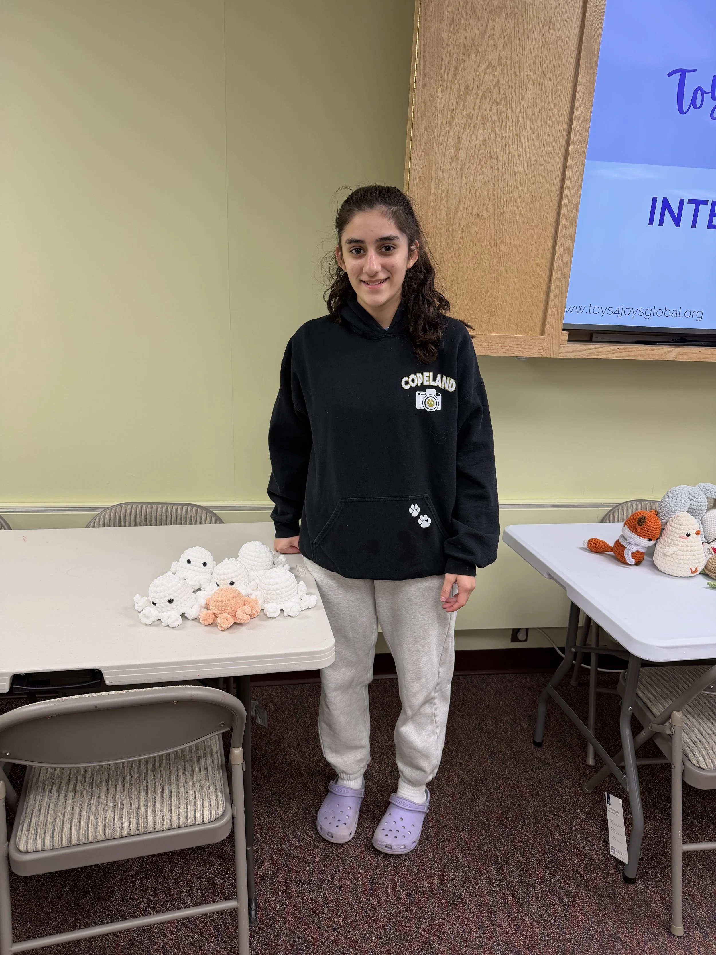 A young woman standing behind a table with amigurumi crochet animals in a room with light green walls.