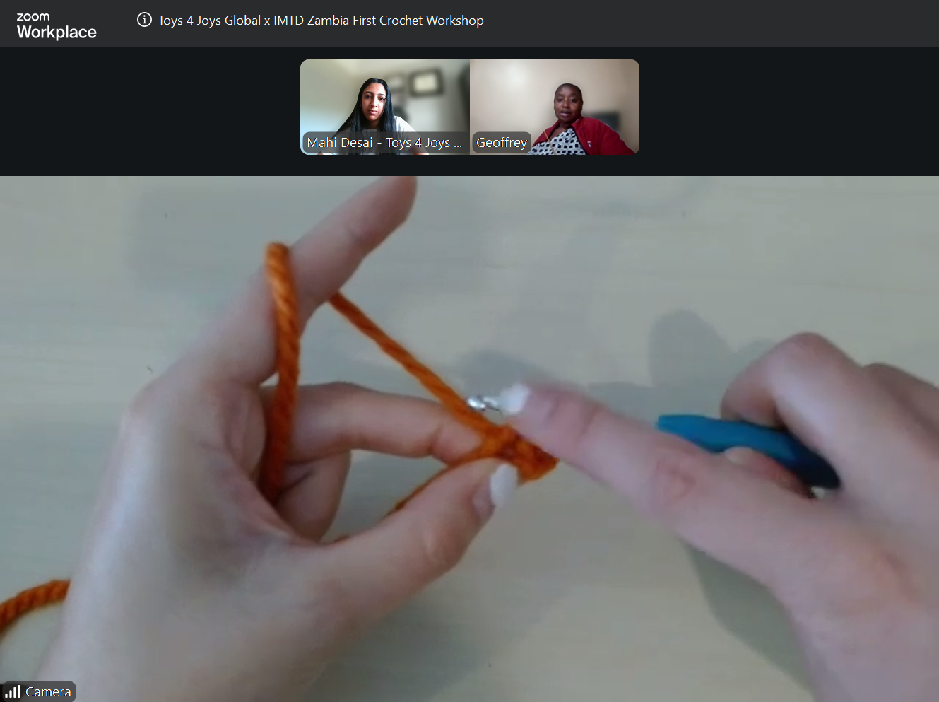 Close-up of hands knitting bright orange yarn with a blue crochet hook during an online workshop.