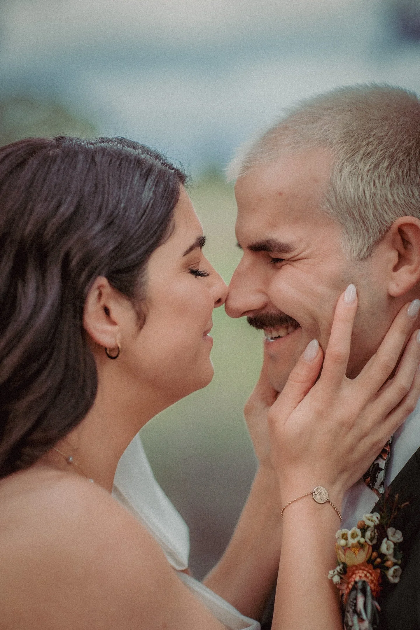 A couple with smiles on their faces, touching foreheads, in a close-up outdoor portrait, celebrating their wedding day.