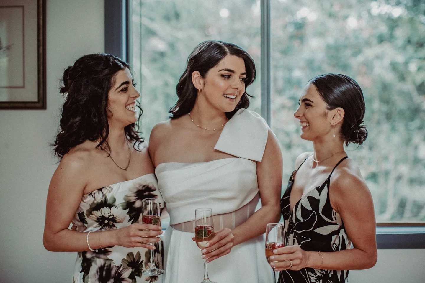 Bride and bridesmaids smiling and chatting while holding glasses of champagne during getting ready.