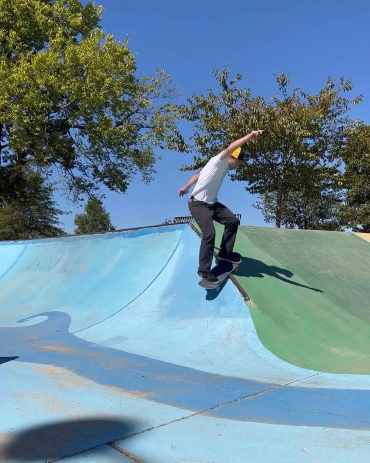 A person skateboarding in a colorful skate park on a sunny day with clear blue sky and green trees in the background.
