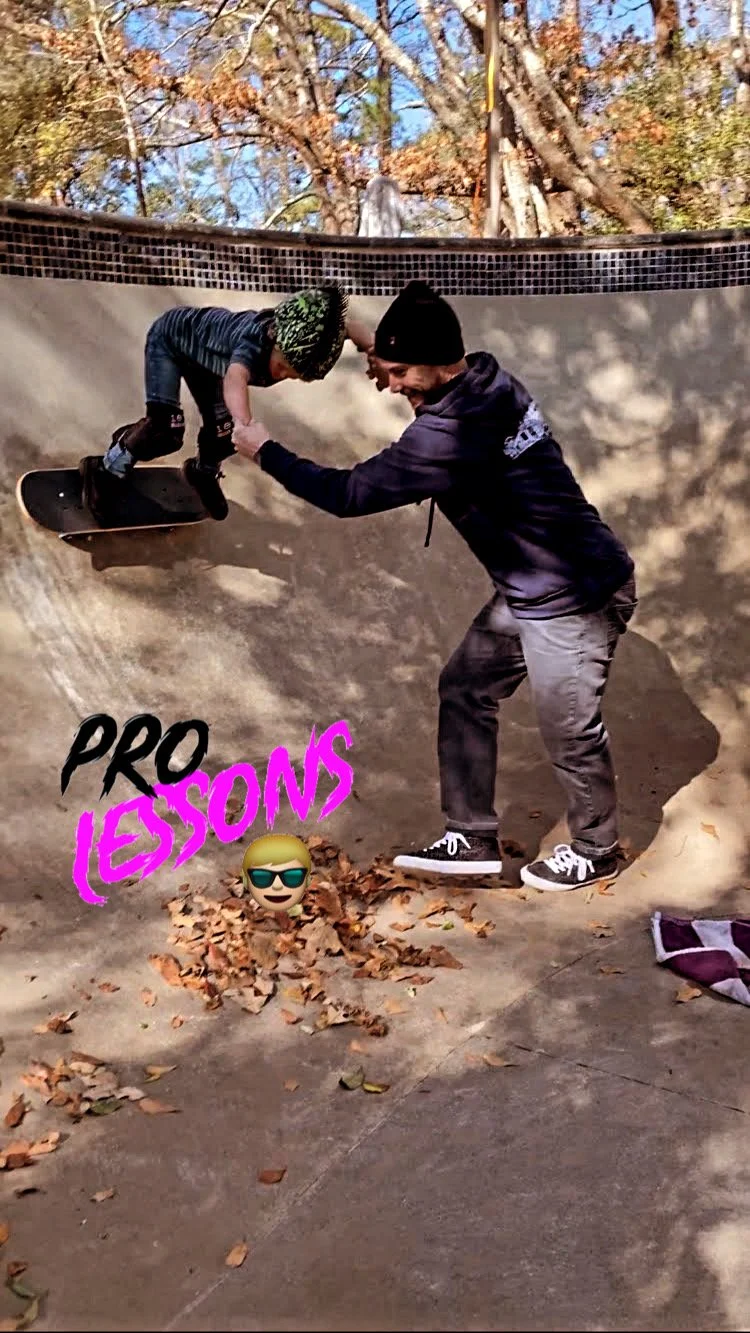 A skateboarder as a young child wearing a green and black beanie being assisted by an adult male in a black beanie at a skate park. The child is on a skateboard inside a concrete skate bowl, with the adult holding the child's hands for support. Fallen leaves are scattered on the ground, and there are trees with autumn foliage in the background. The photo has a sticker that says "Pro Lessons" with a selfie emoji wearing sunglasses.