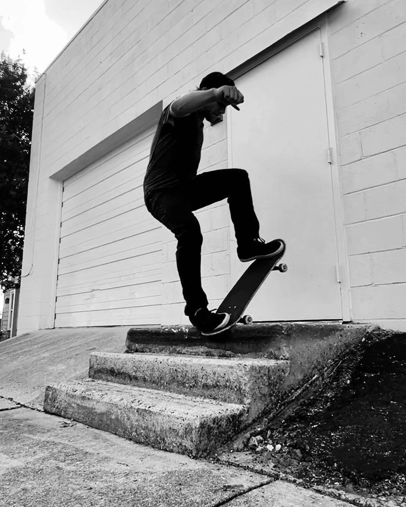 A person performing a skateboard trick on a set of concrete stairs outside. The image is in black and white.