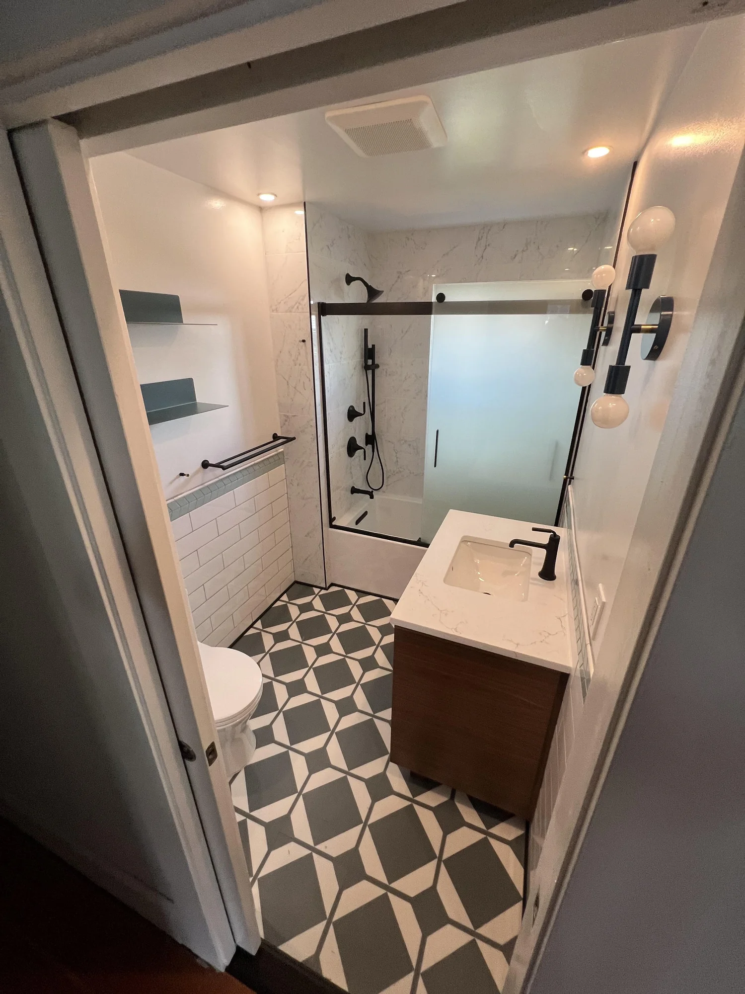 Chad's bathroom with glass shower, white tile and patterned floor