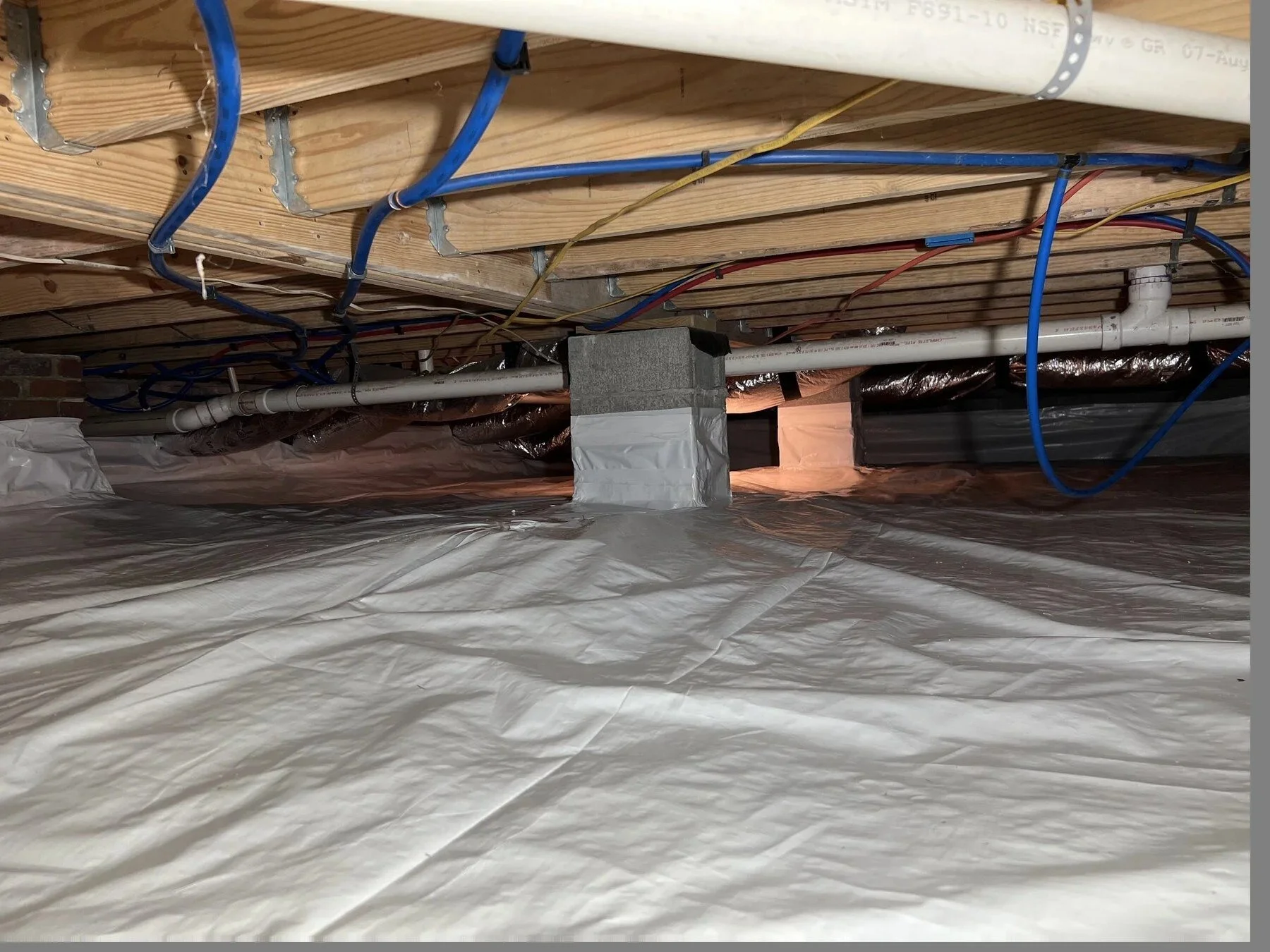 Crawl space with plumbing, wiring and ductwork over a plastic vapor barrier in Murfreesboro, Tennessee.